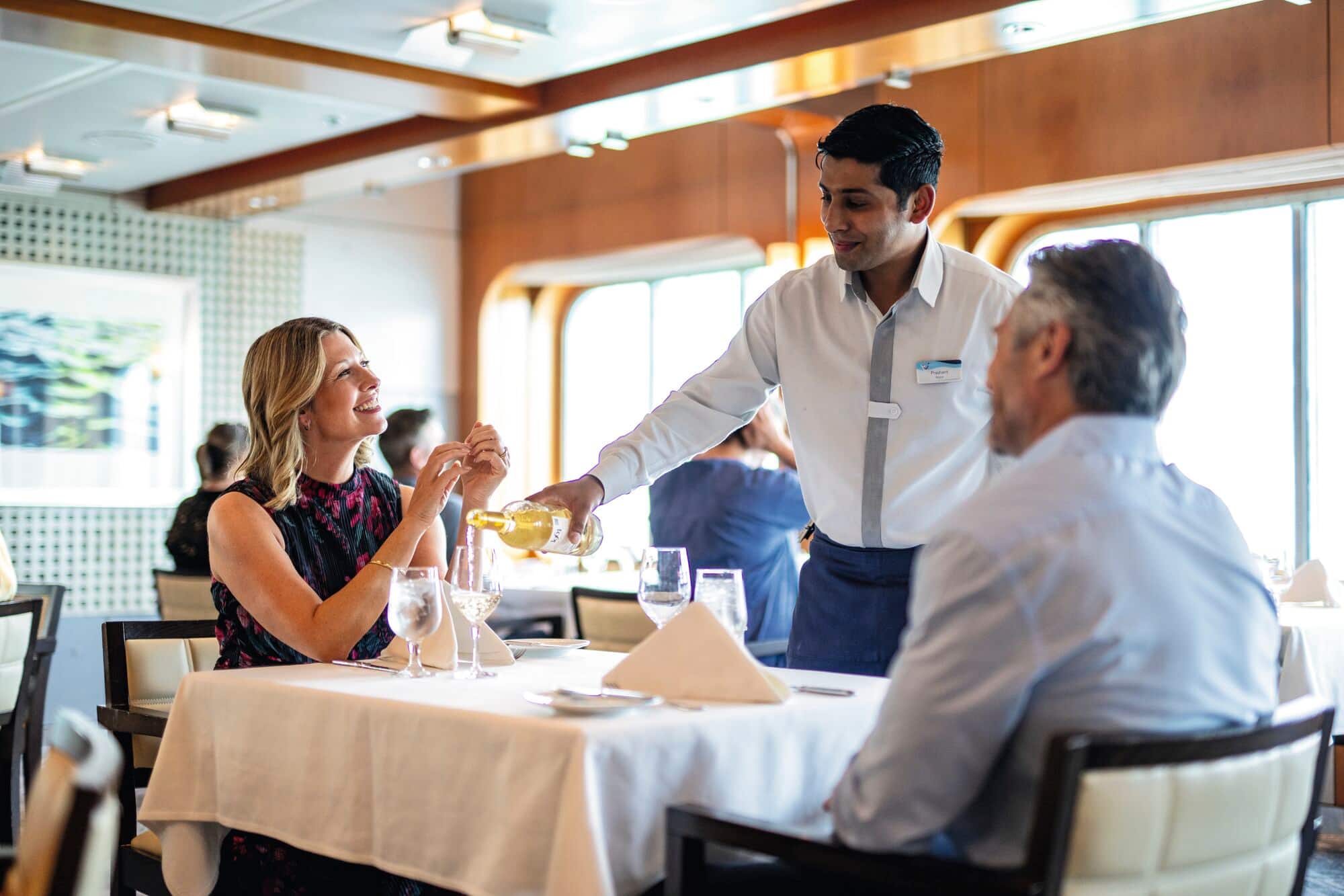 A waiter pouring drinks for a couple at a dining table.