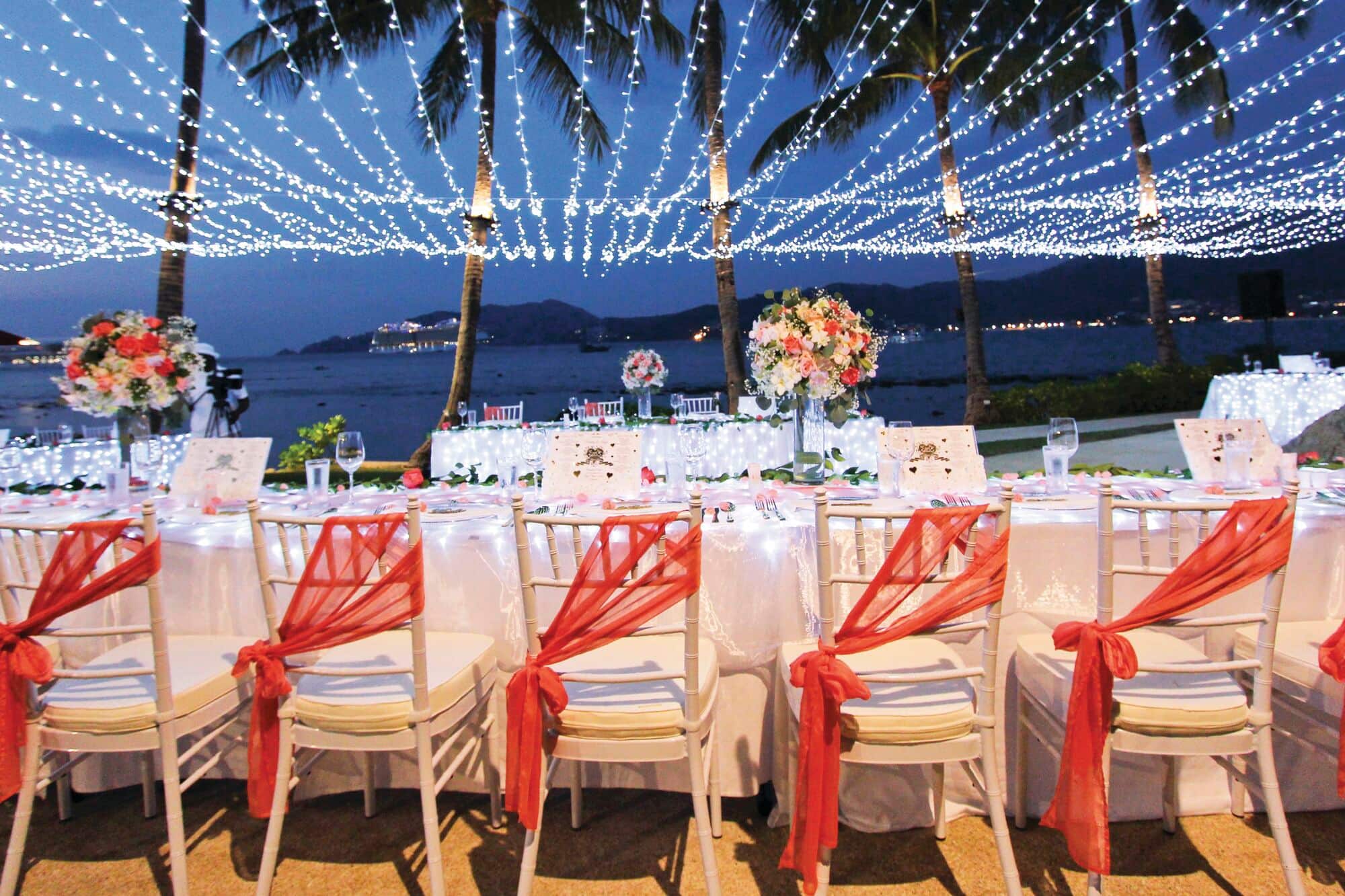 Twinkling lights illuminate a seaside wedding reception set-up at night.