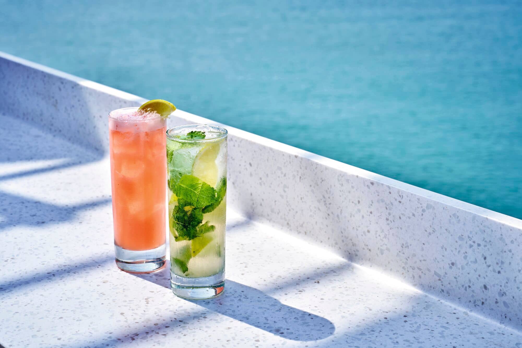 A pair of tall cocktail glasses beside a swimming pool.