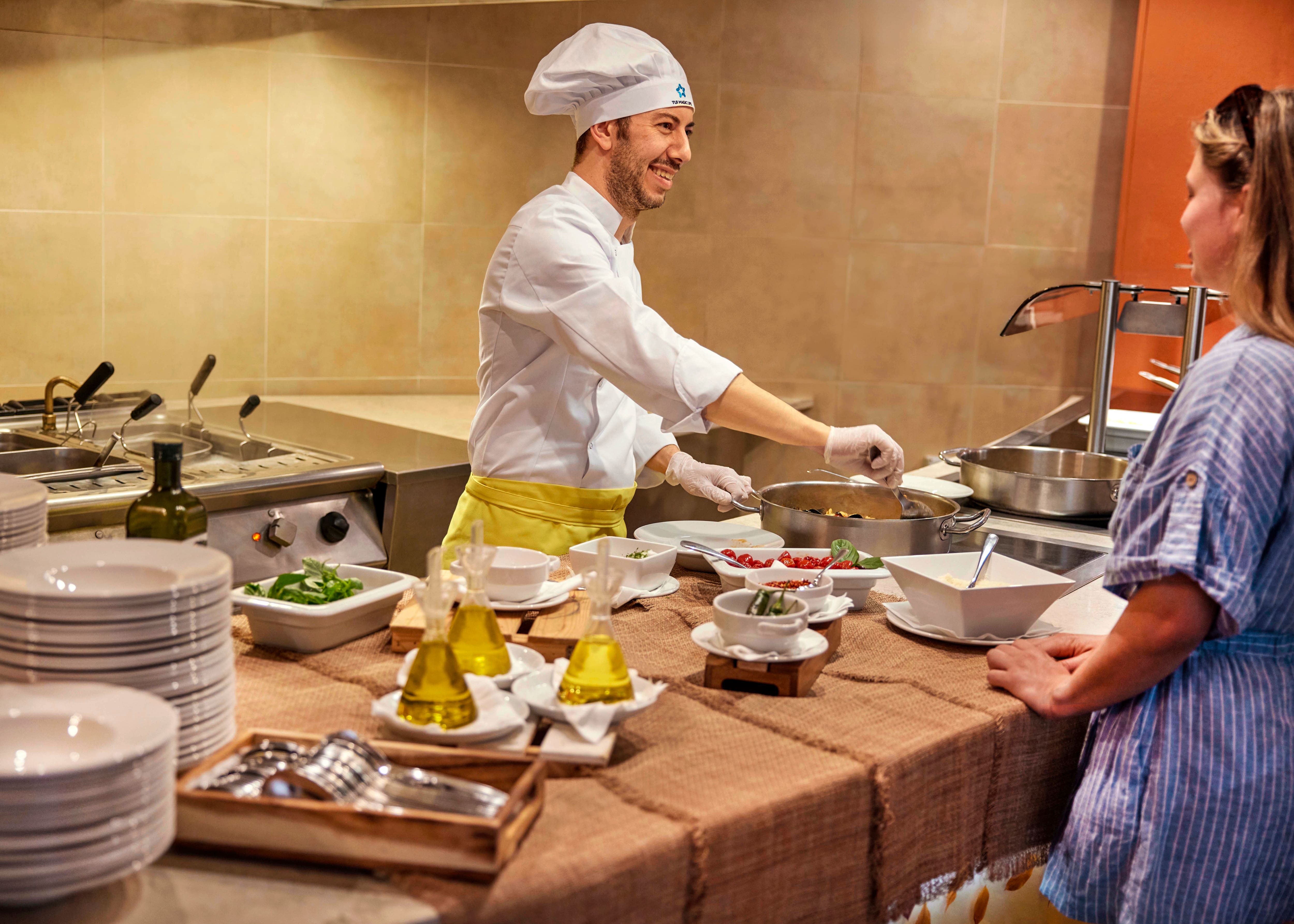 Chef cooking in front of hotel guest and smiling.
