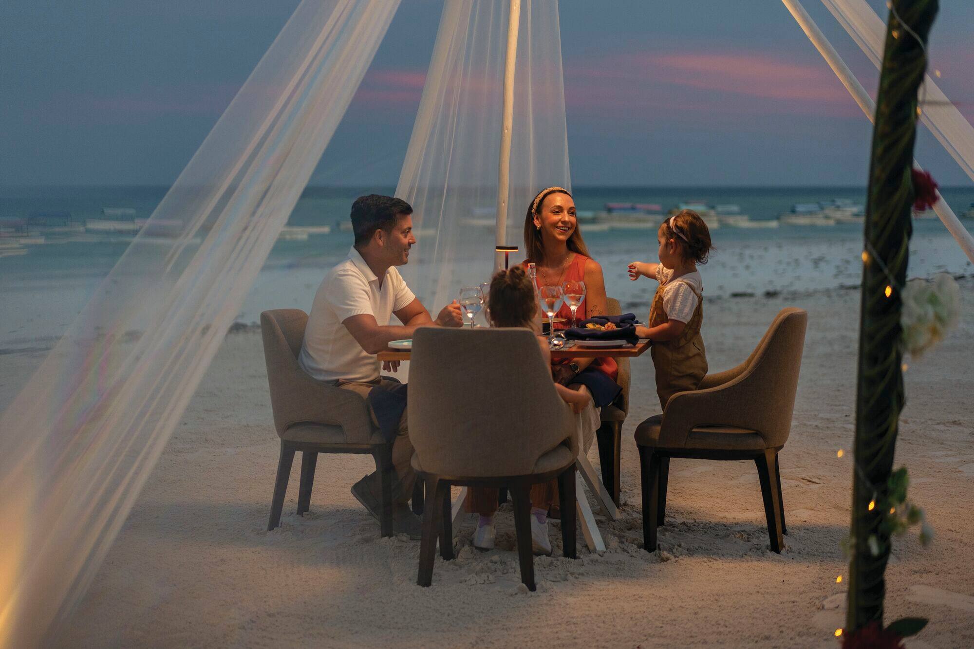 A family sit at an al fresco dinner table on the beach.