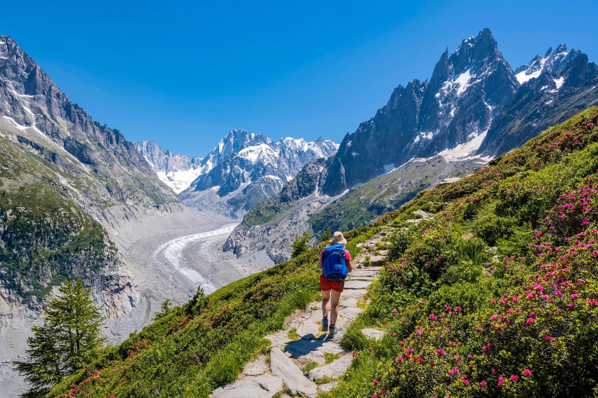 A woman seen from behind walking up a hiking path in the French mountains with a glacier visible in the distance.