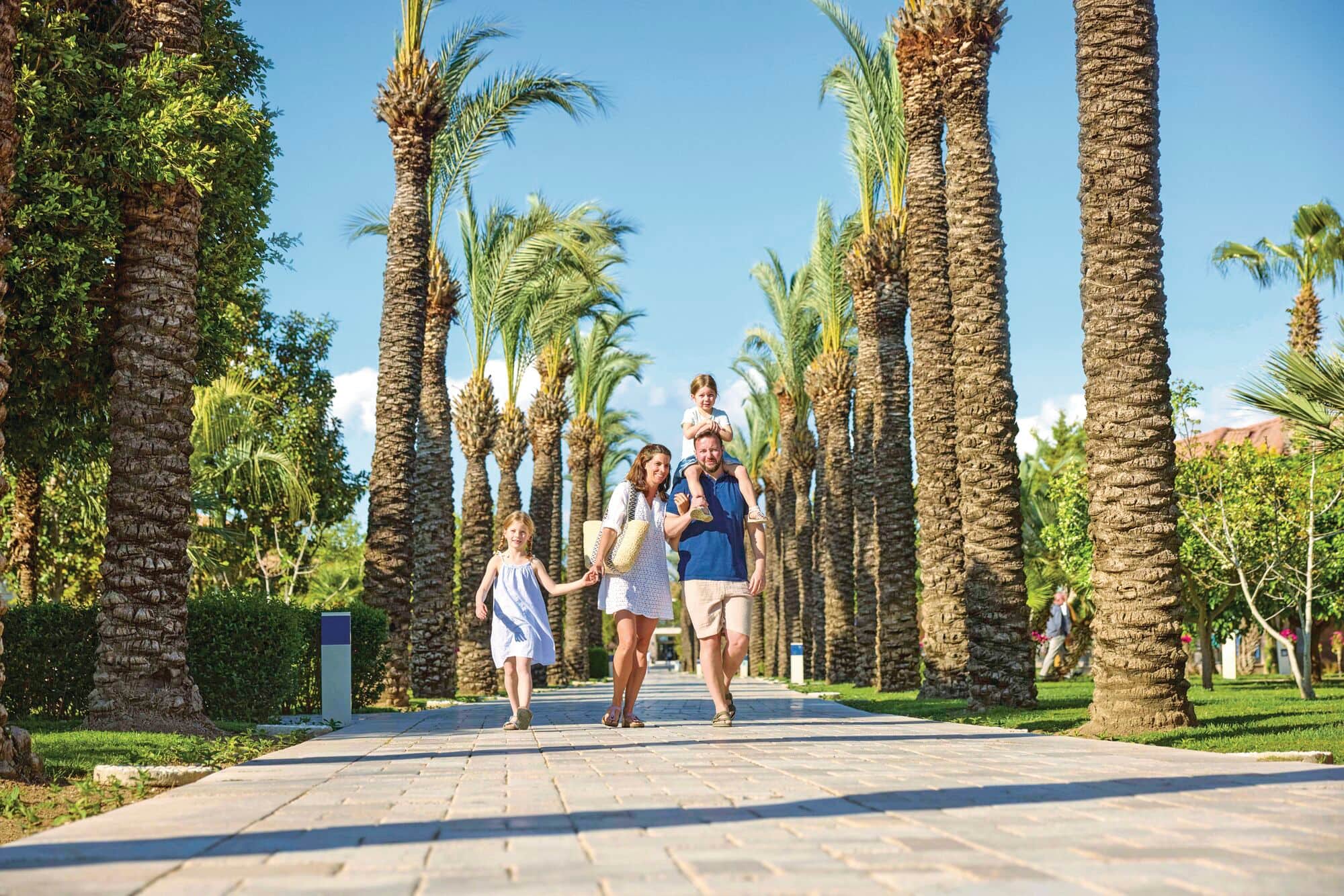 A family of 4 walking along a palm-fringed hotel garden.