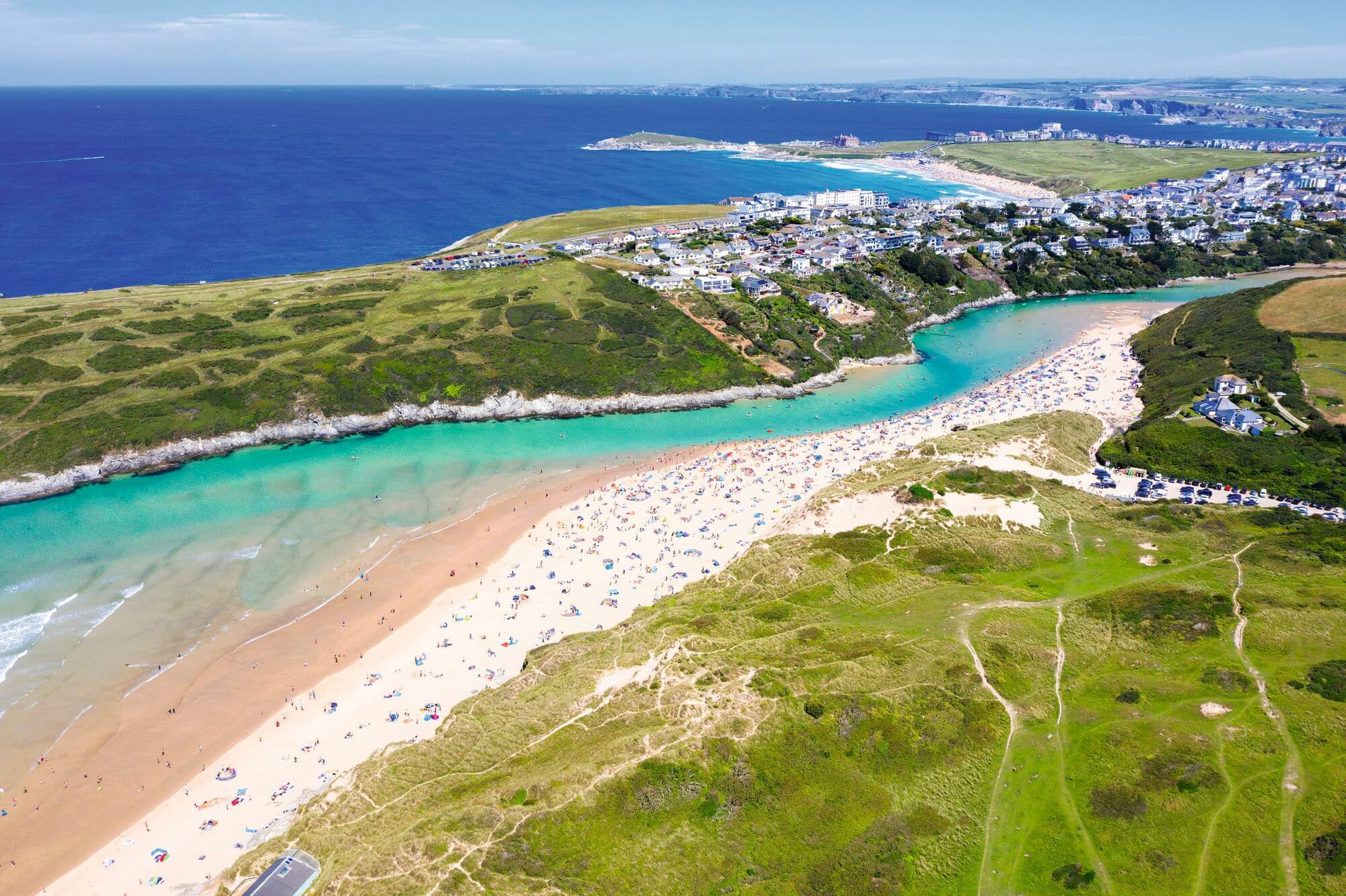 Wide shot of a long, sandy beach surrounded by countryside in Newquay.