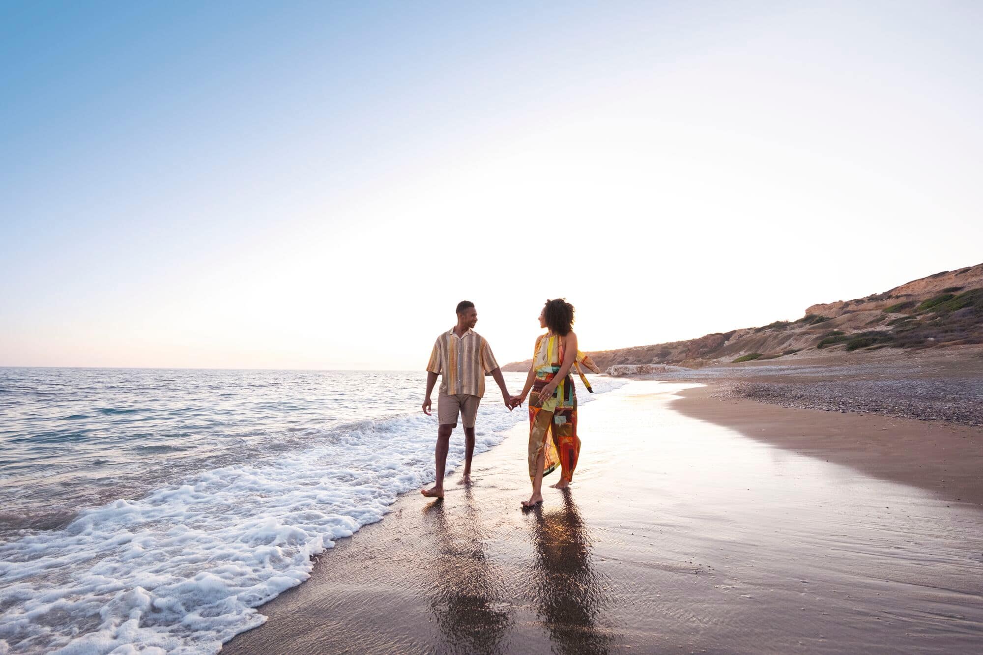 Couple walking along a beach at sunset.