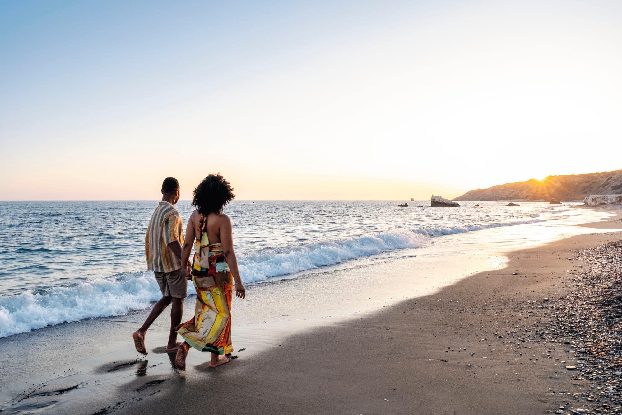 A couple walking along a beach at sunset.