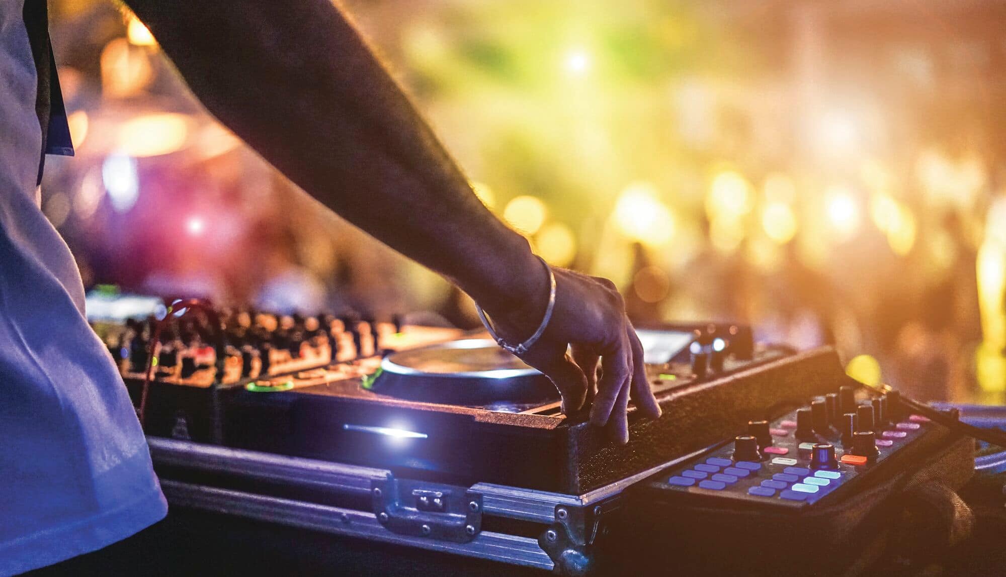 Person operating a DJ mixing deck at an event with blurred lights in the background.