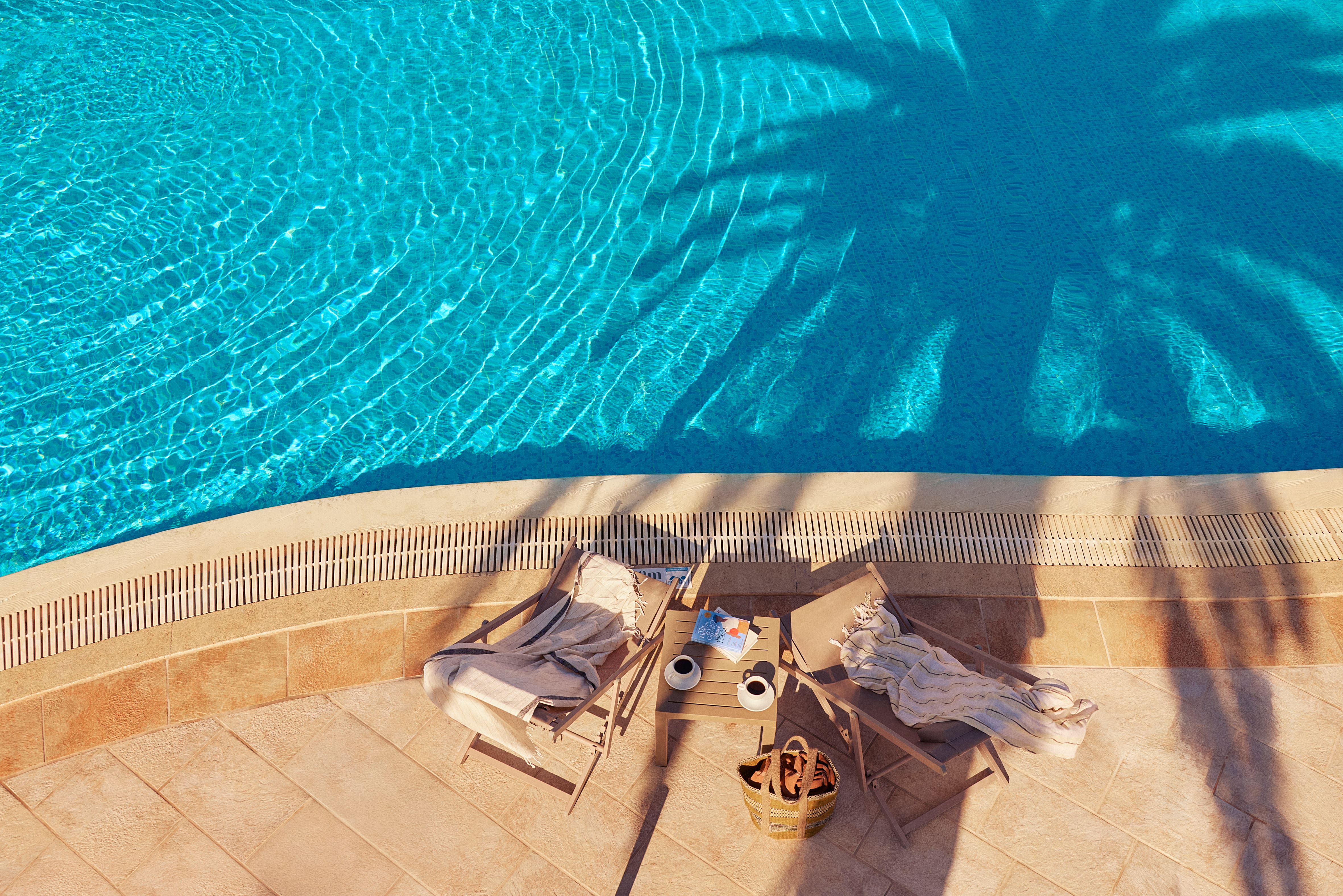Top-down view of two deck chairs placed side-by-side next to a swimming pool in Crete, Greece.