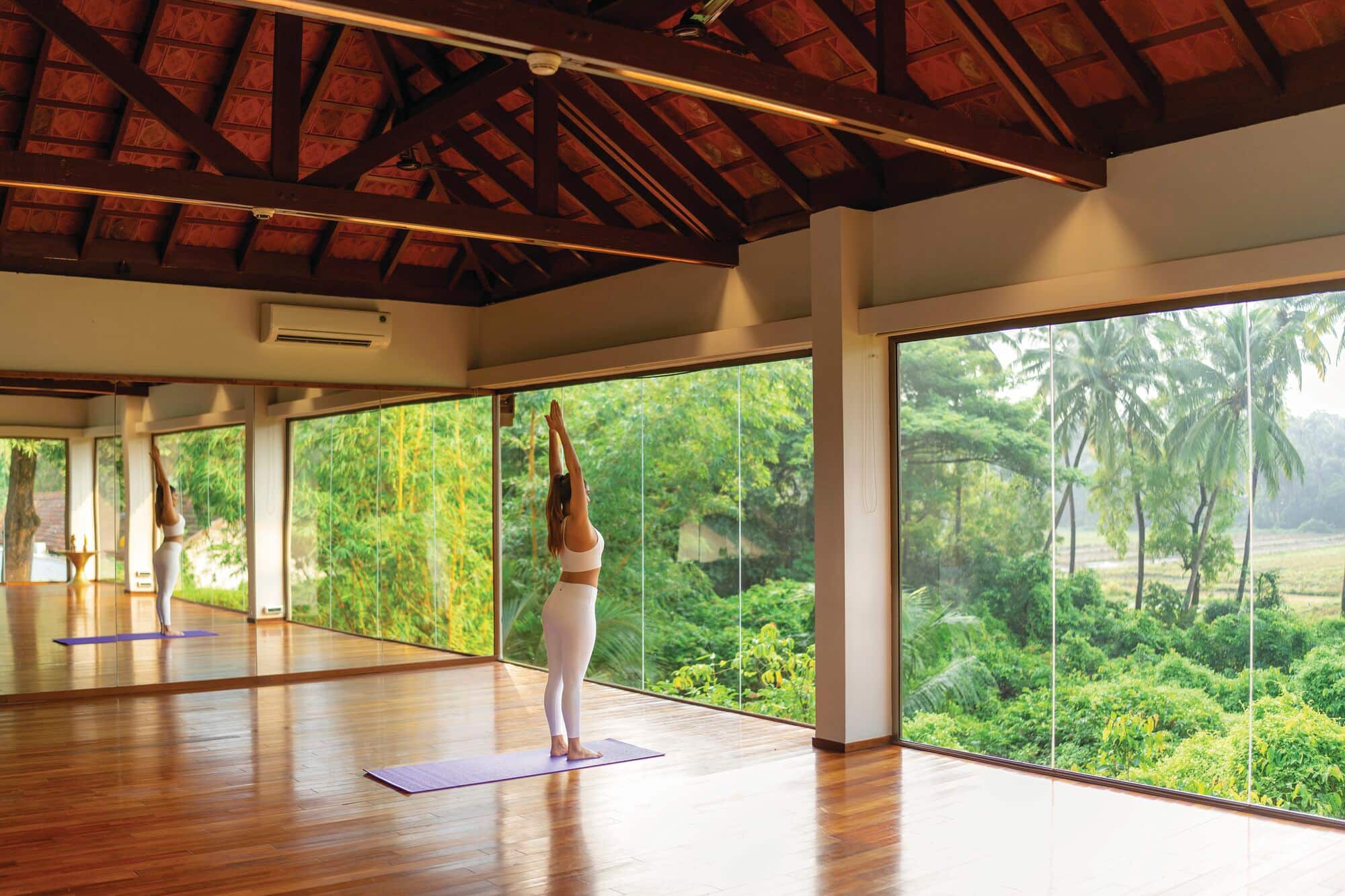 A guest practising yoga in a light-filled studio overlooking tropical gardens at The Diwa Club by Alila.