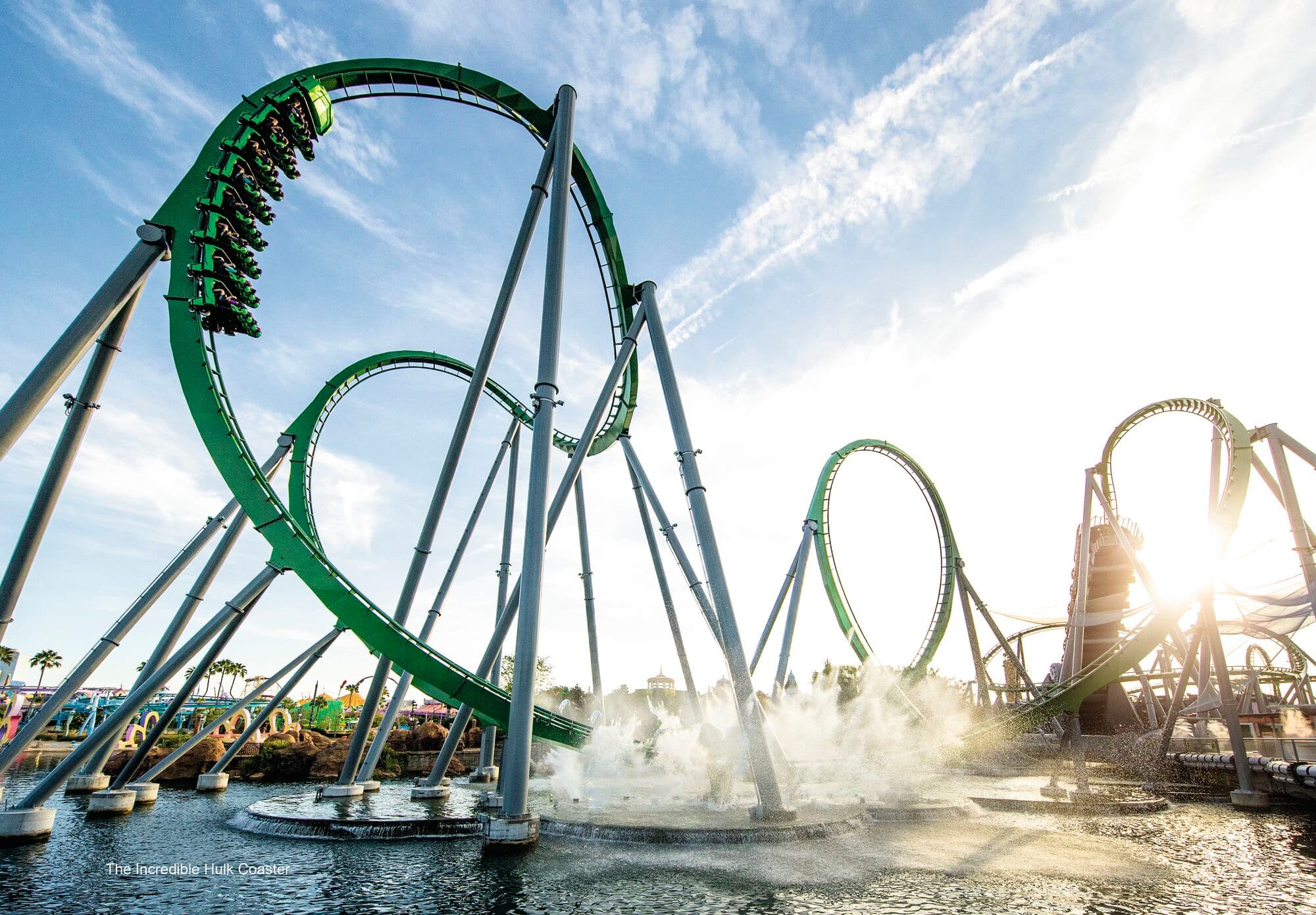 Looping green coaster and water mist under blue skies – thrills, chills and theme park vibes.