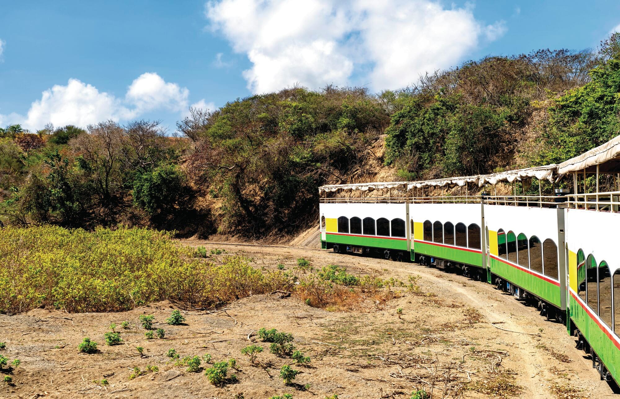 The tourist double decker scenic railway train travels along tracks through the tropical rural landscape of Saint Kitts island in the Caribbean.