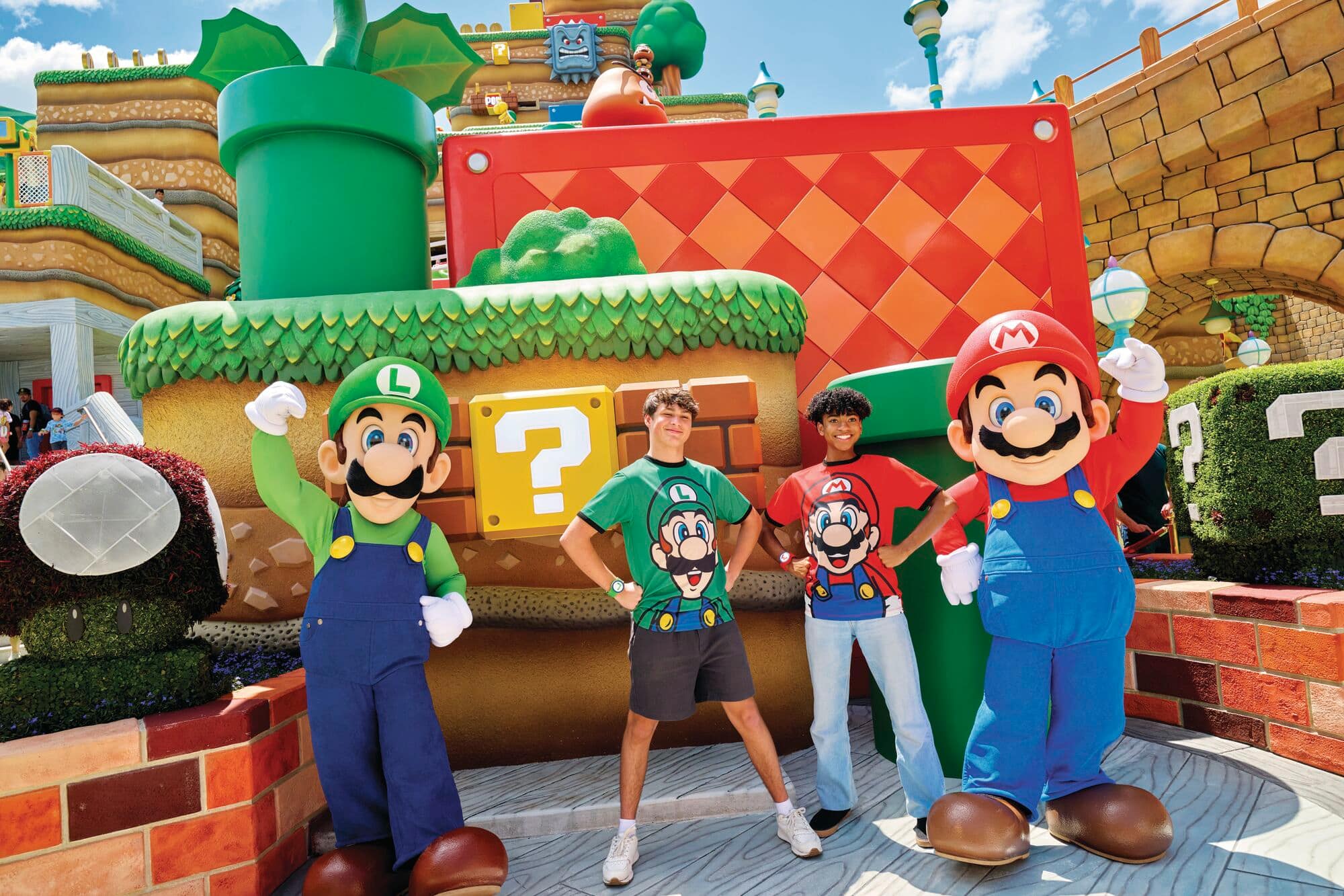 Two teens standing next to Mario and Luigi at Super Nintendo World.