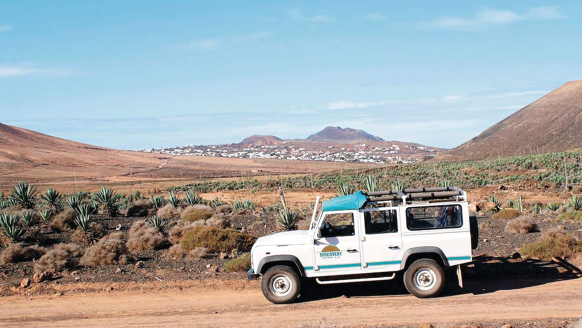 Jeep crossing desert with volcanic hills in the distance.