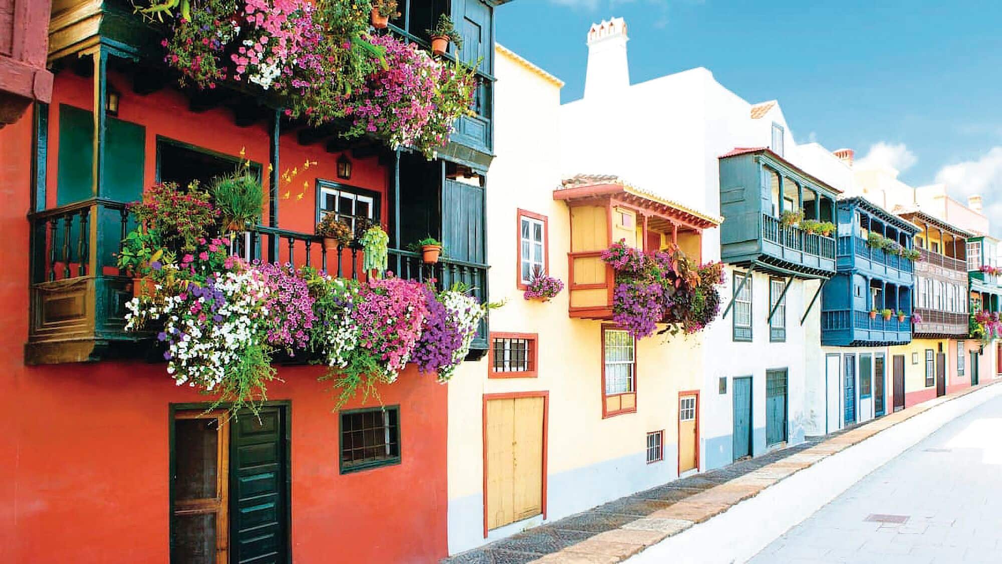 Row of colourful houses with wooden balconies decorated with hanging flowers.