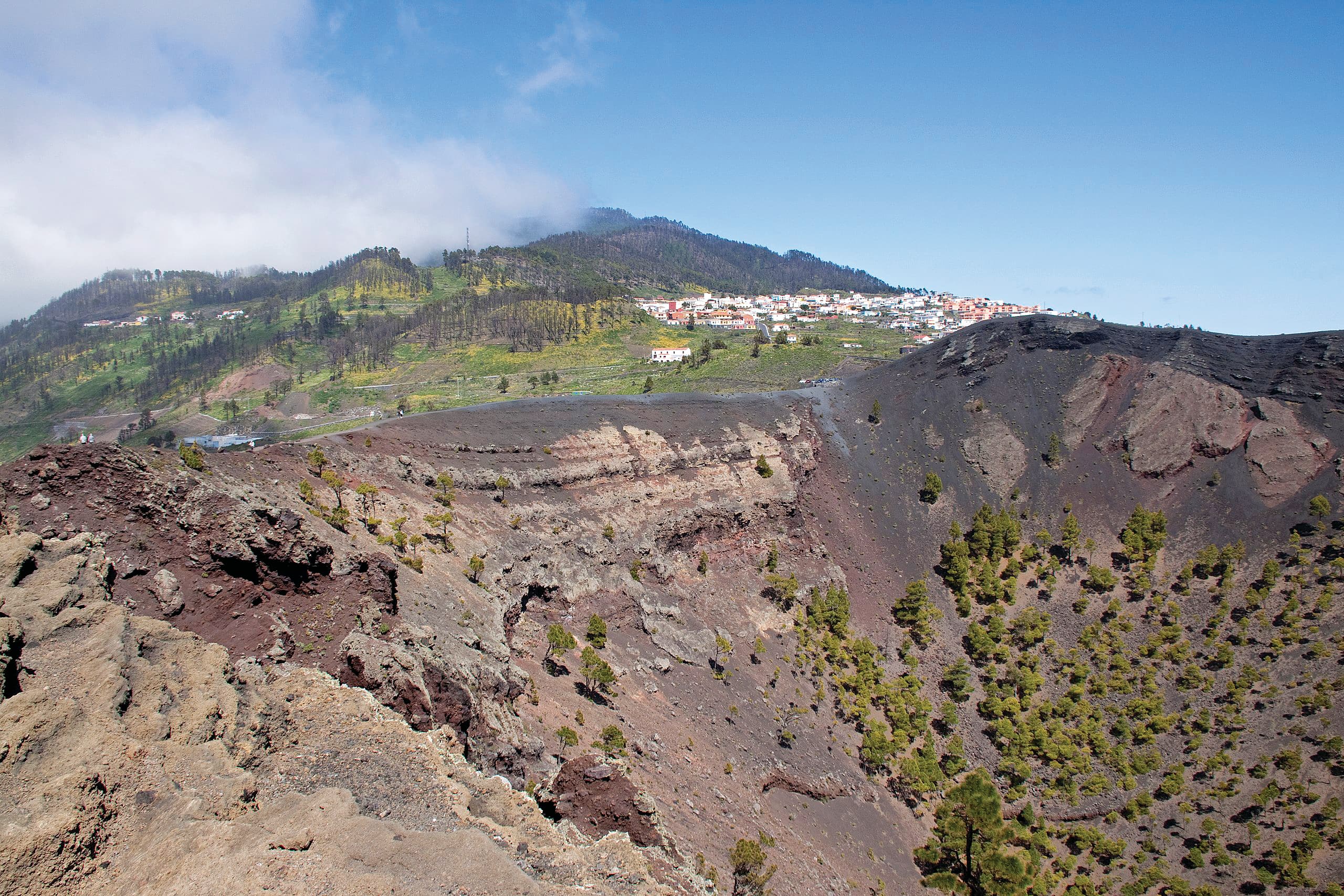 Volcanic crater with a sunny hillside village in the distance.