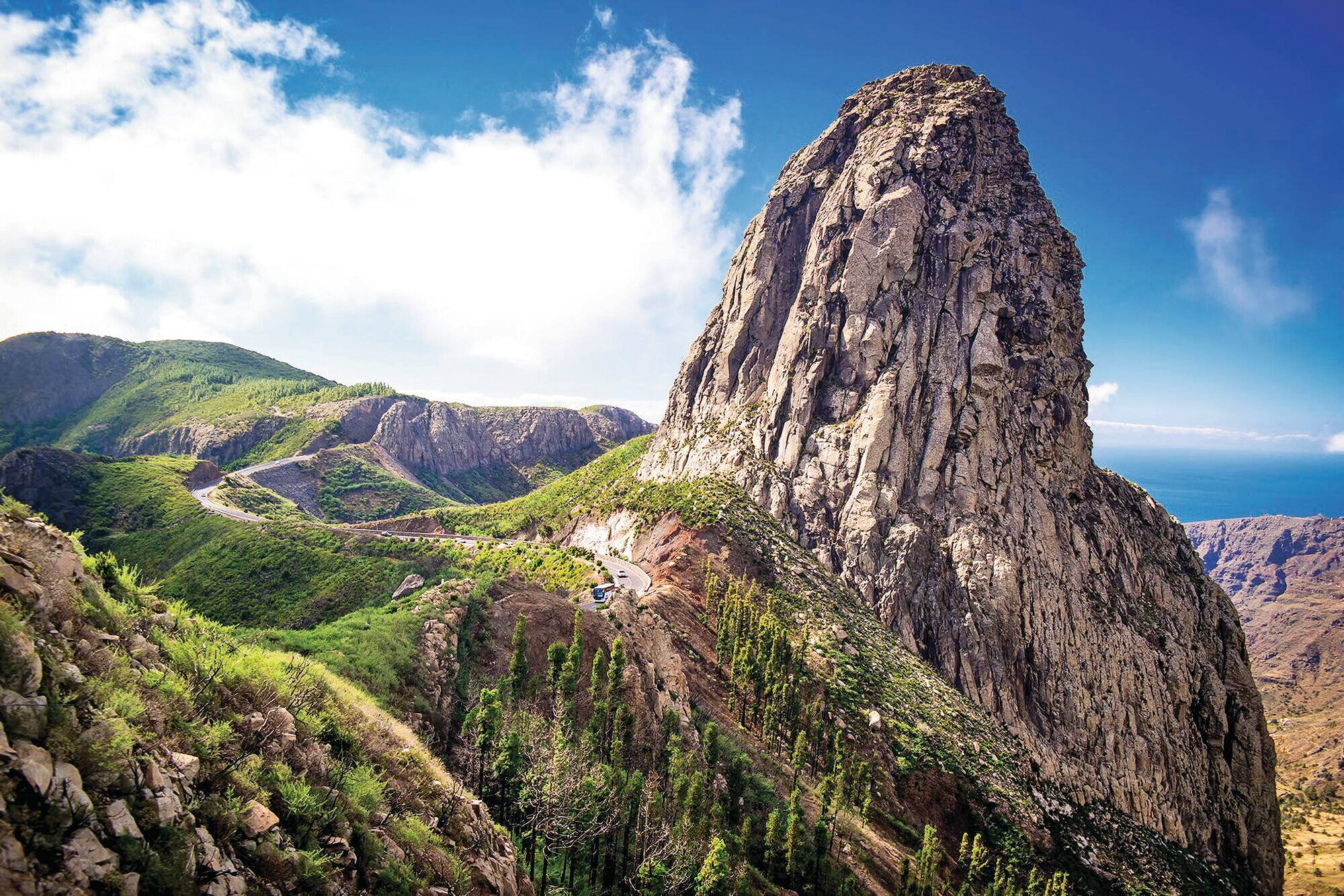 Steep rocky peak rising above green mountain slopes.