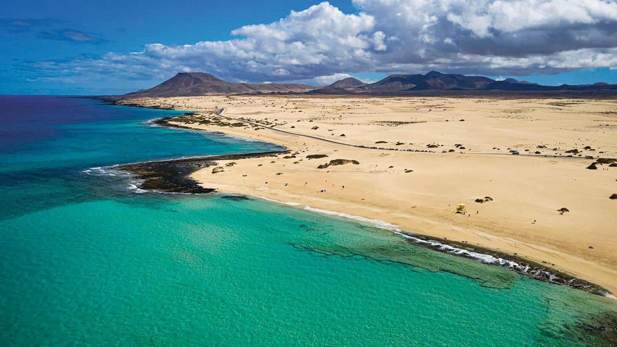 Sandy beach with turquoise water and volcanic mountains.