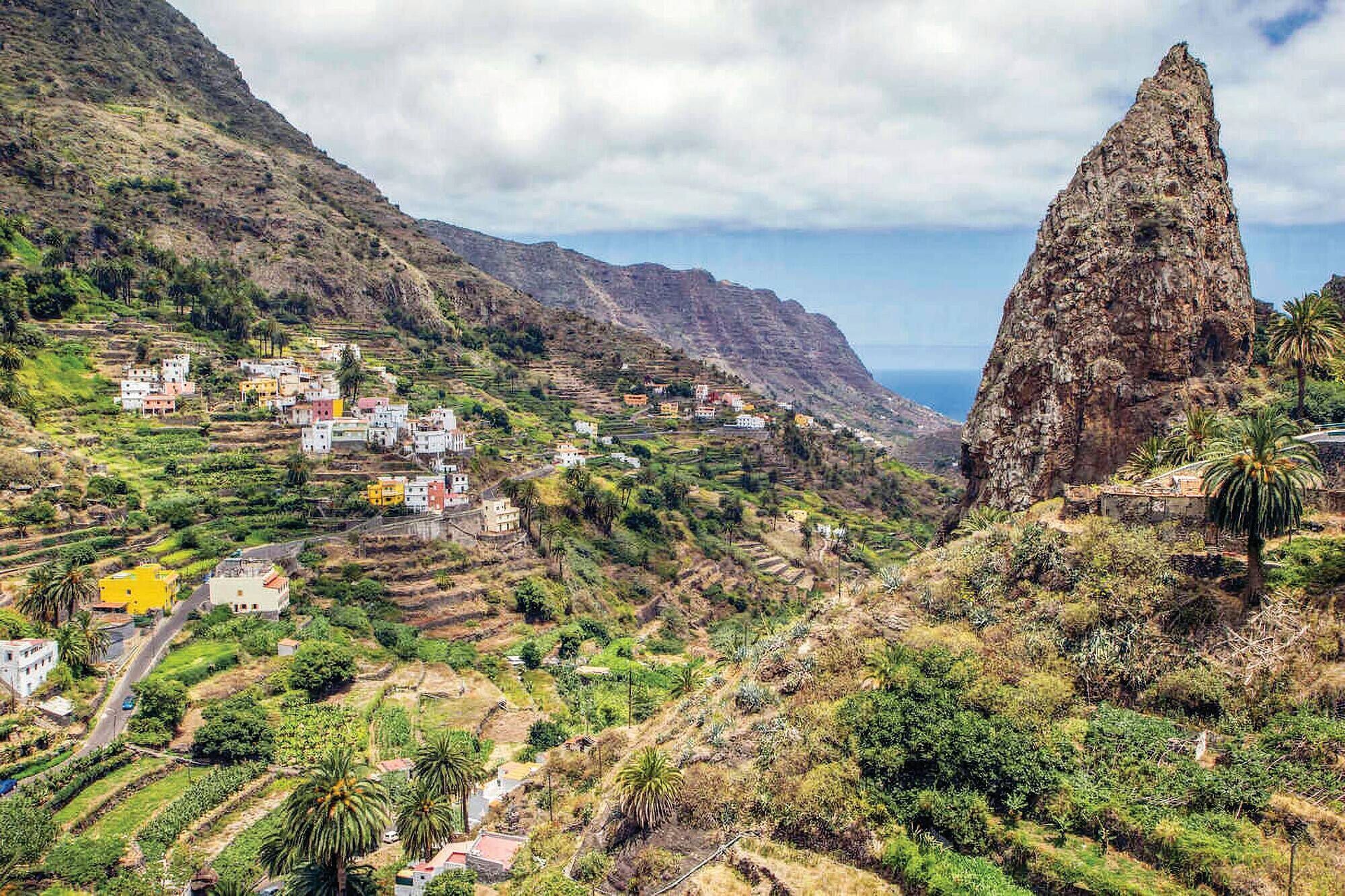 Green valley with colourful hillside houses and a rock formation overlooking the sea.