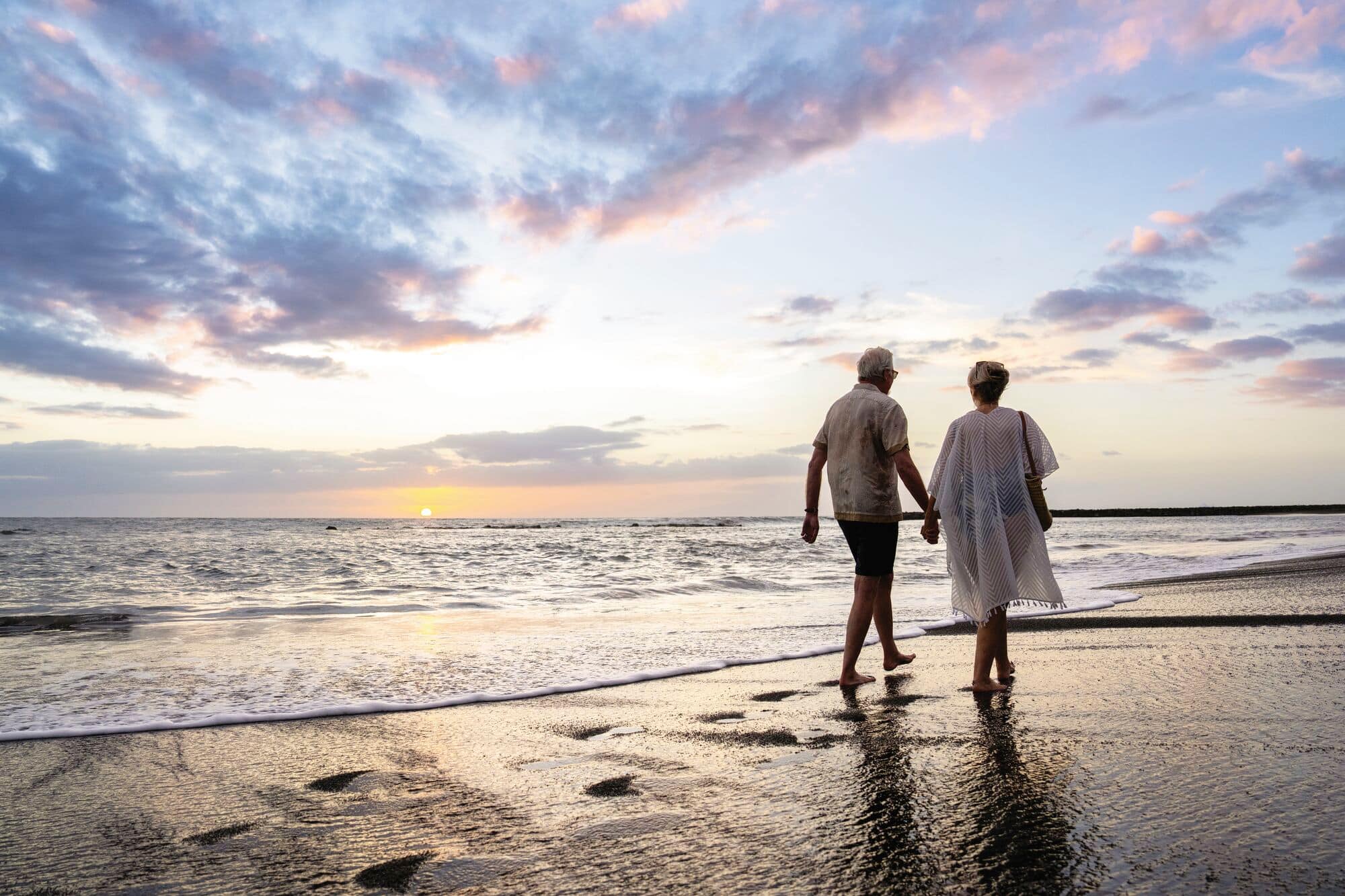 A mature couple walking along a beach at sunset.