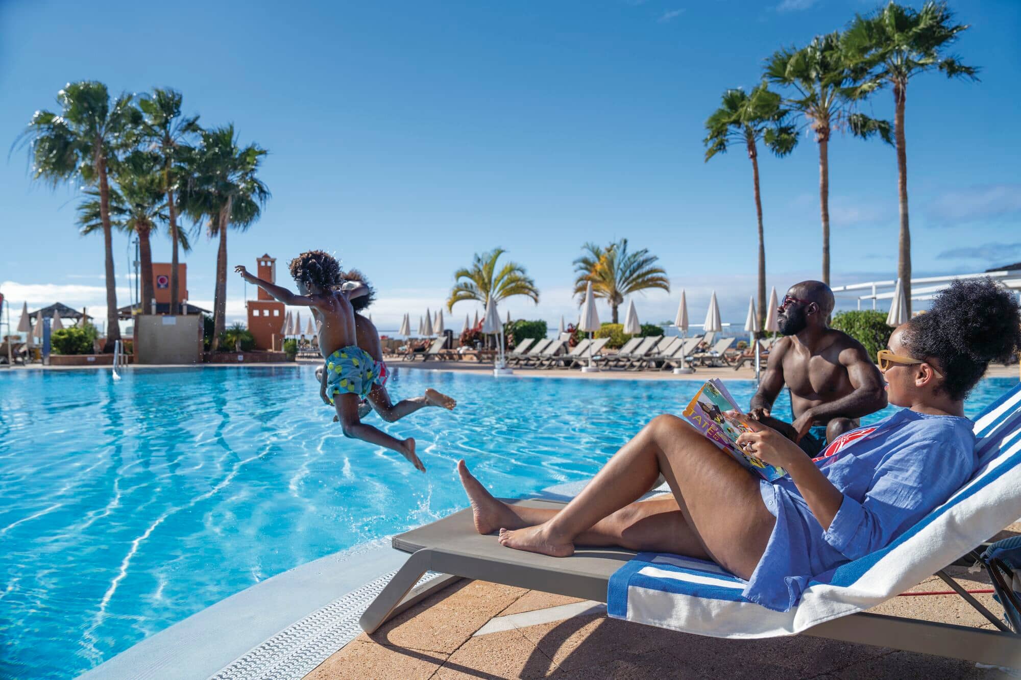 A mum and Dad watching children jumping into hotel pool.
