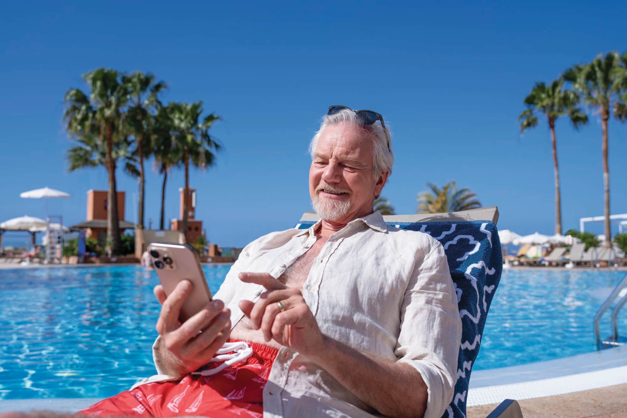 A man relaxing and using her phone on a poolside sun lounger. 