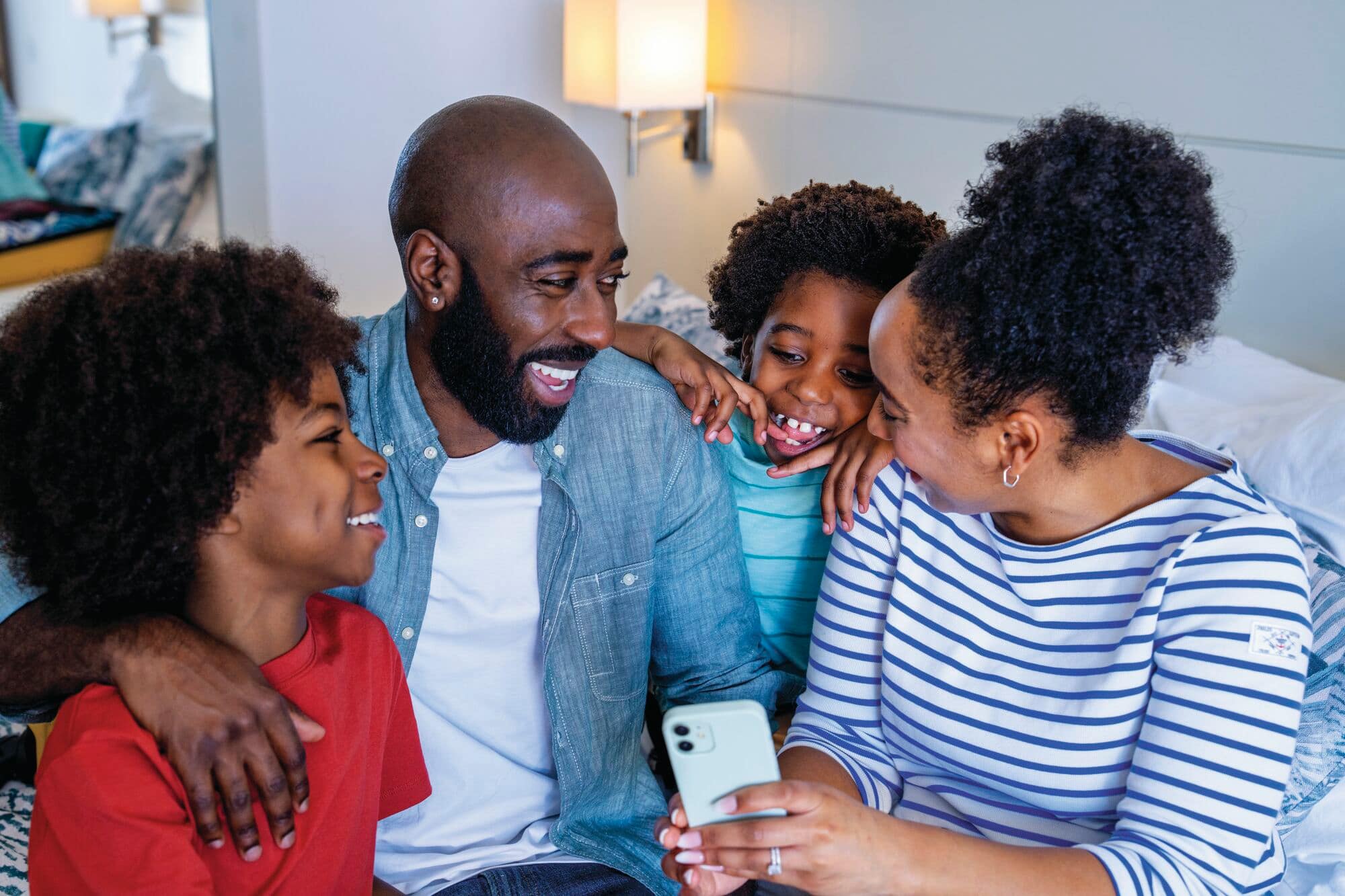 A family of four smiling and looking at holidays on a phone.