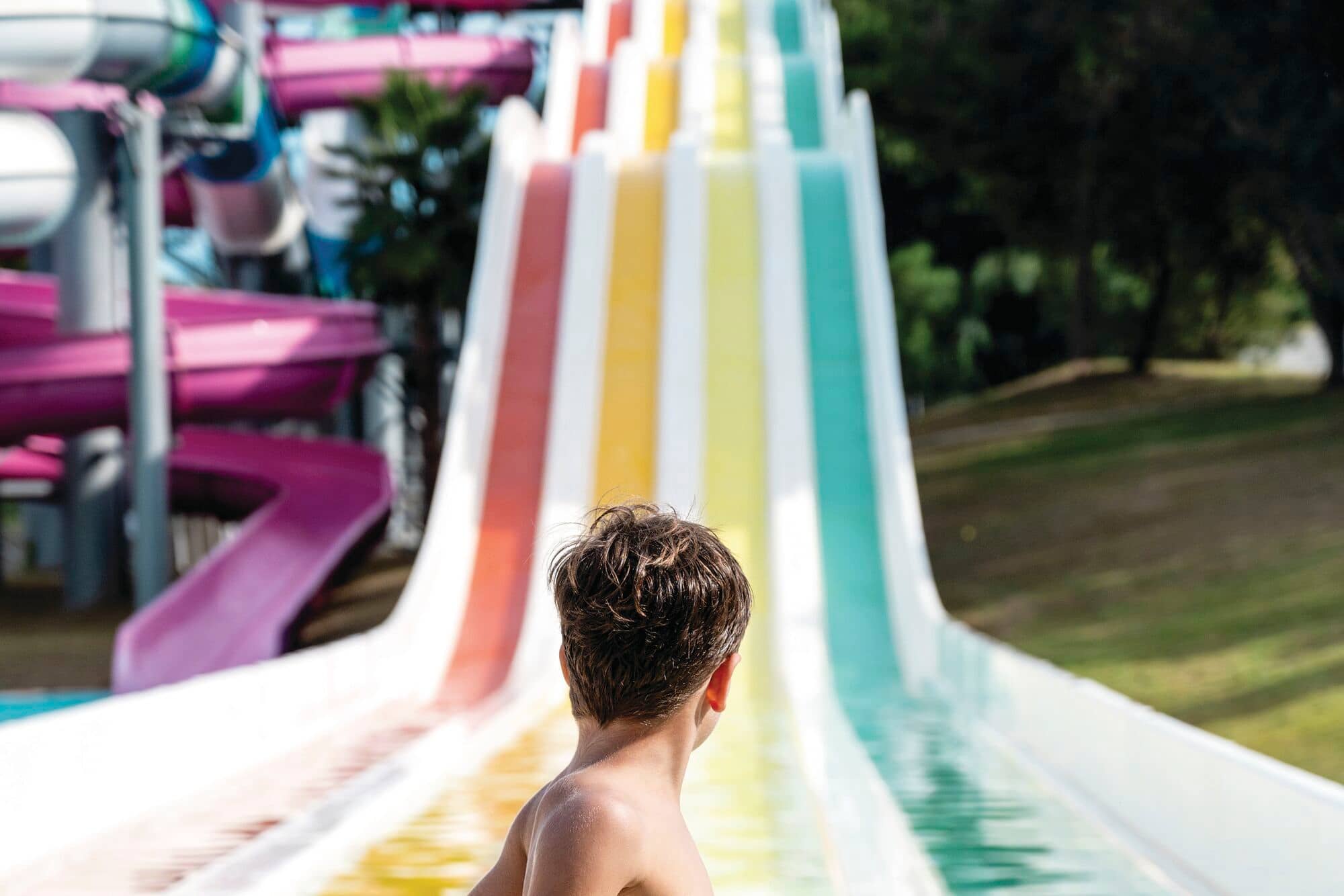 A child at the bottom of a colourful waterslide.