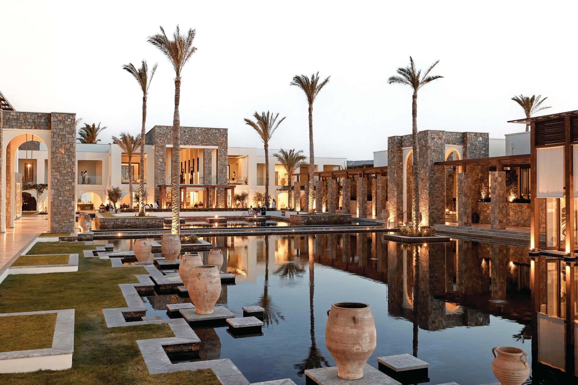 Dusk view of luxury resort with large reflecting pool mirroring cream-colored buildings with Middle Eastern-inspired architecture.