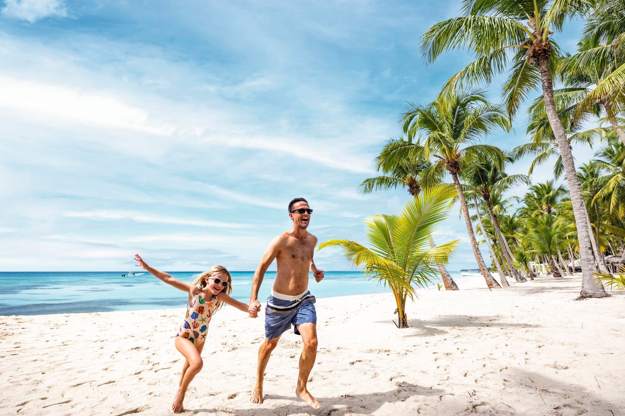 A father and daughter running along a beach smiling.