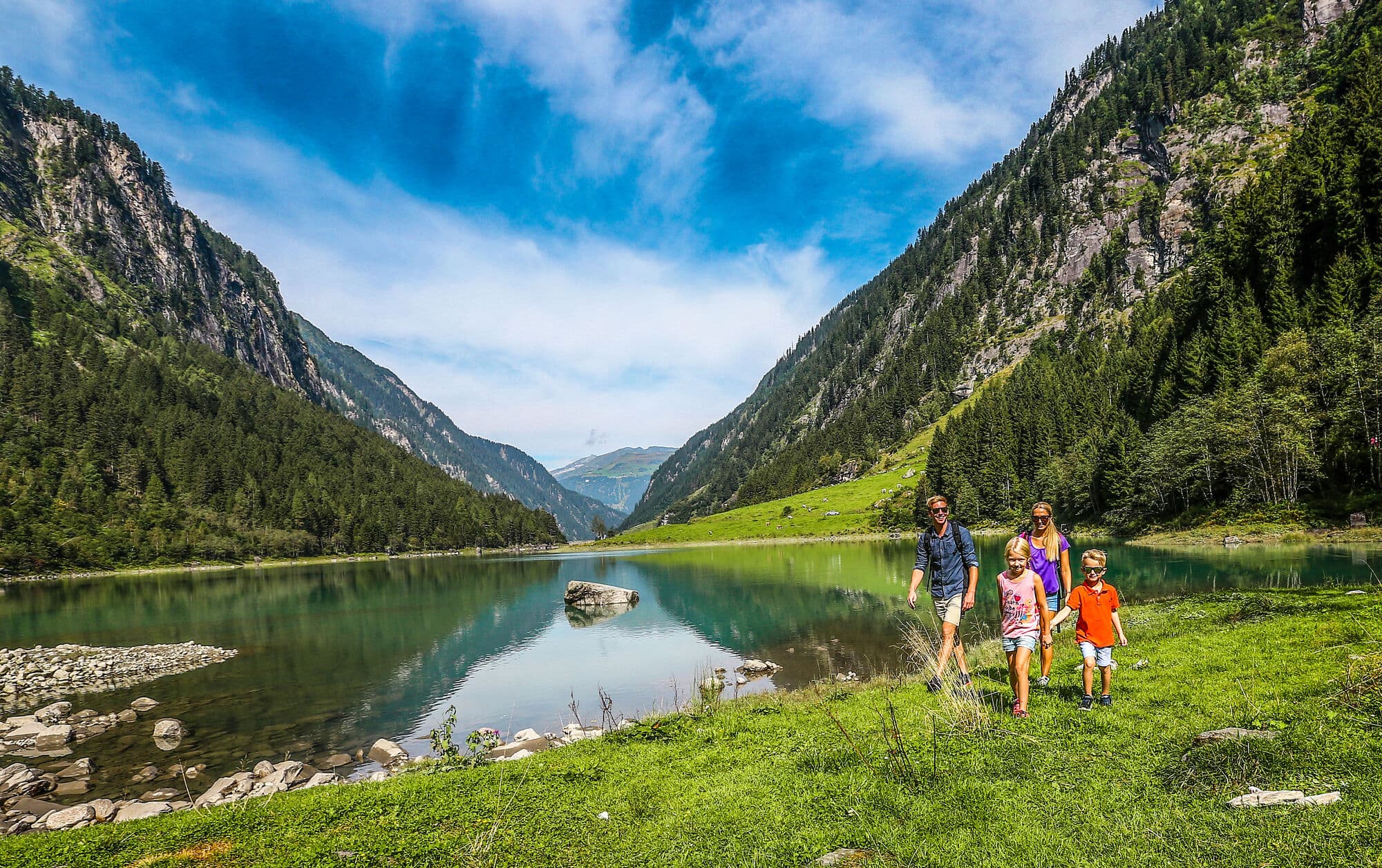 Two adults and two children walking beside a mountain lake in Austria. 