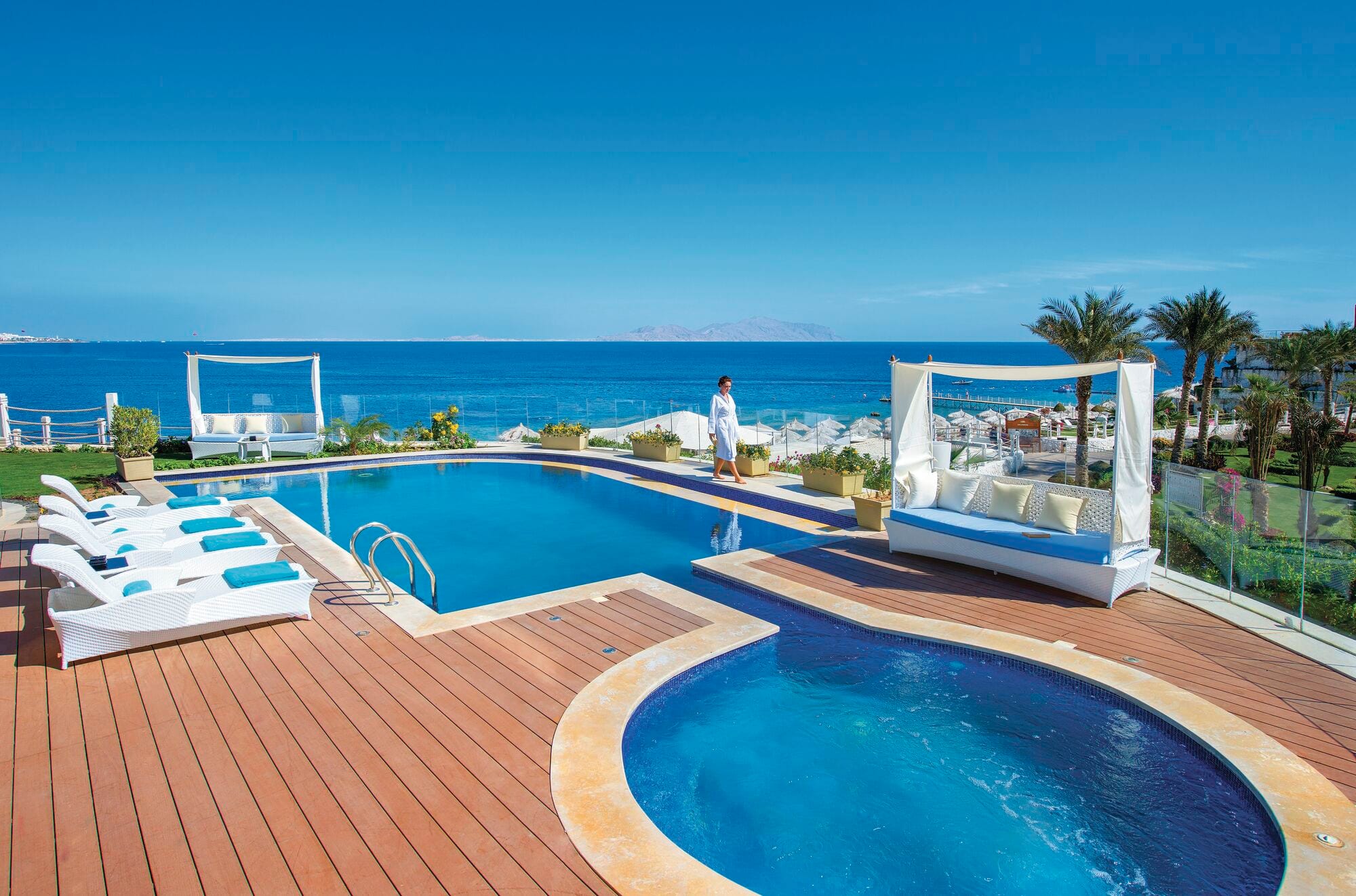 An infinity pool with a sea view and surrounding palm trees.