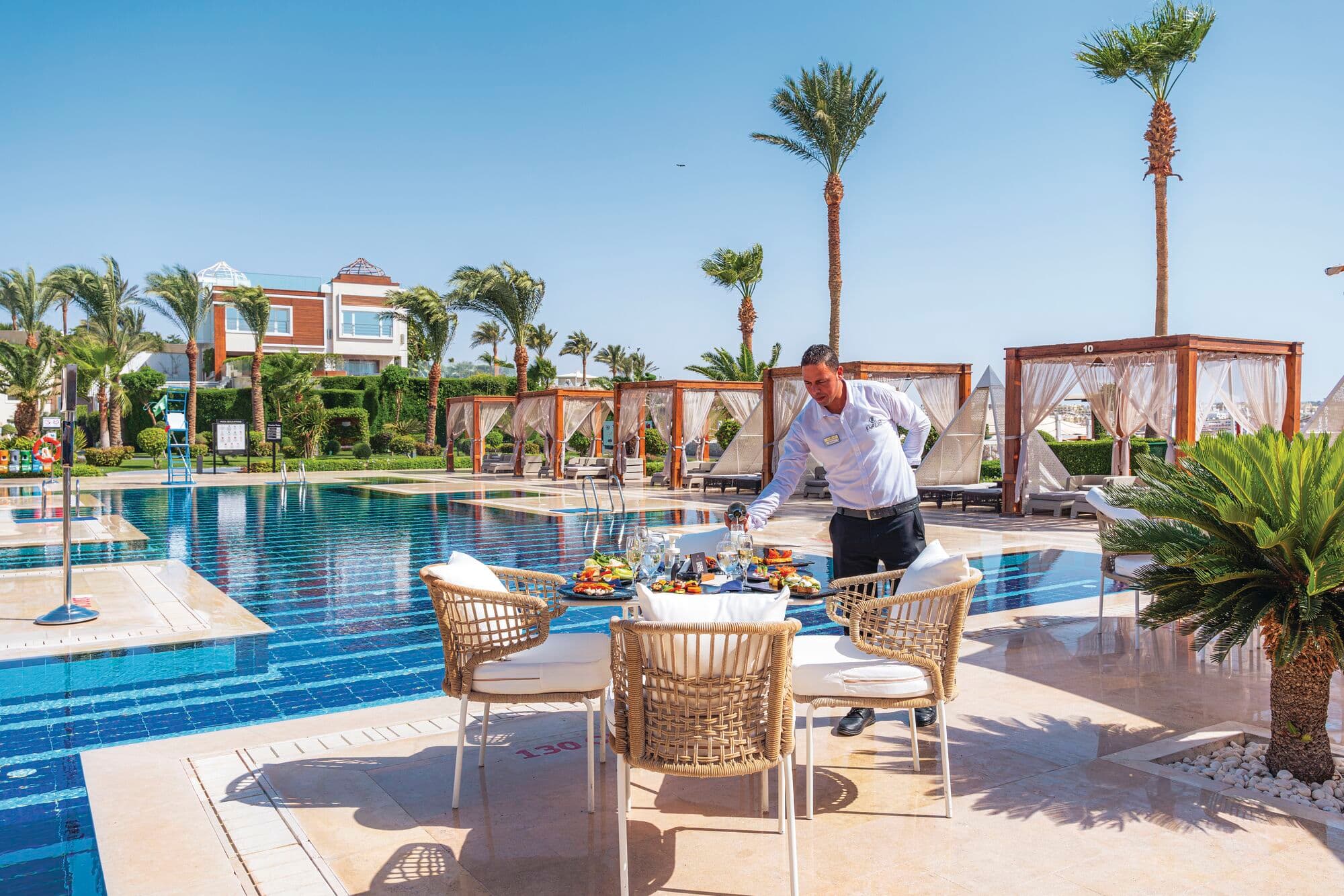 A waiter setting out a table of food by the pool.