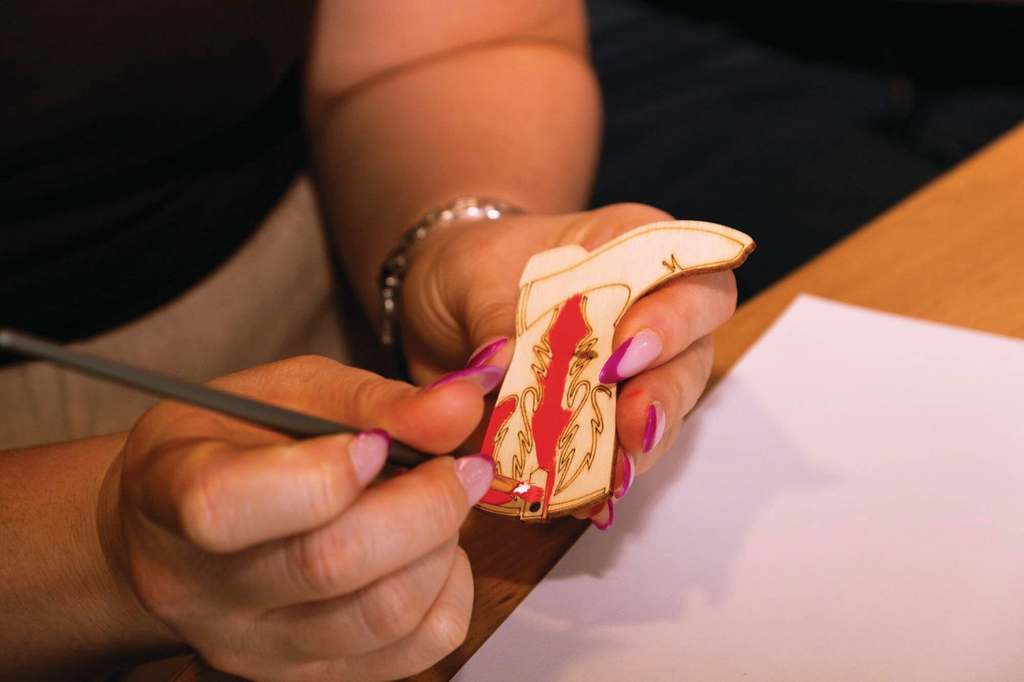 A close-up of a person painting a wooden cowboy boot.