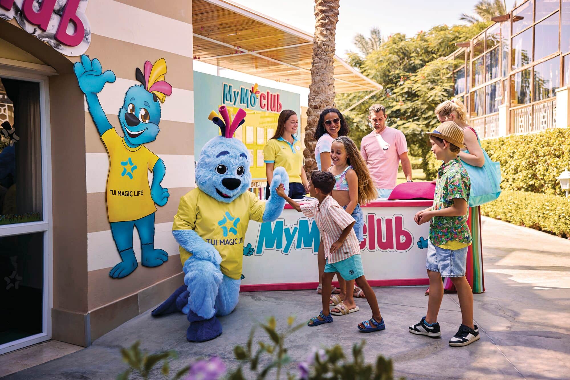 MyMo Club at outdoor resort with blue mascot character in yellow vest interacting with children.