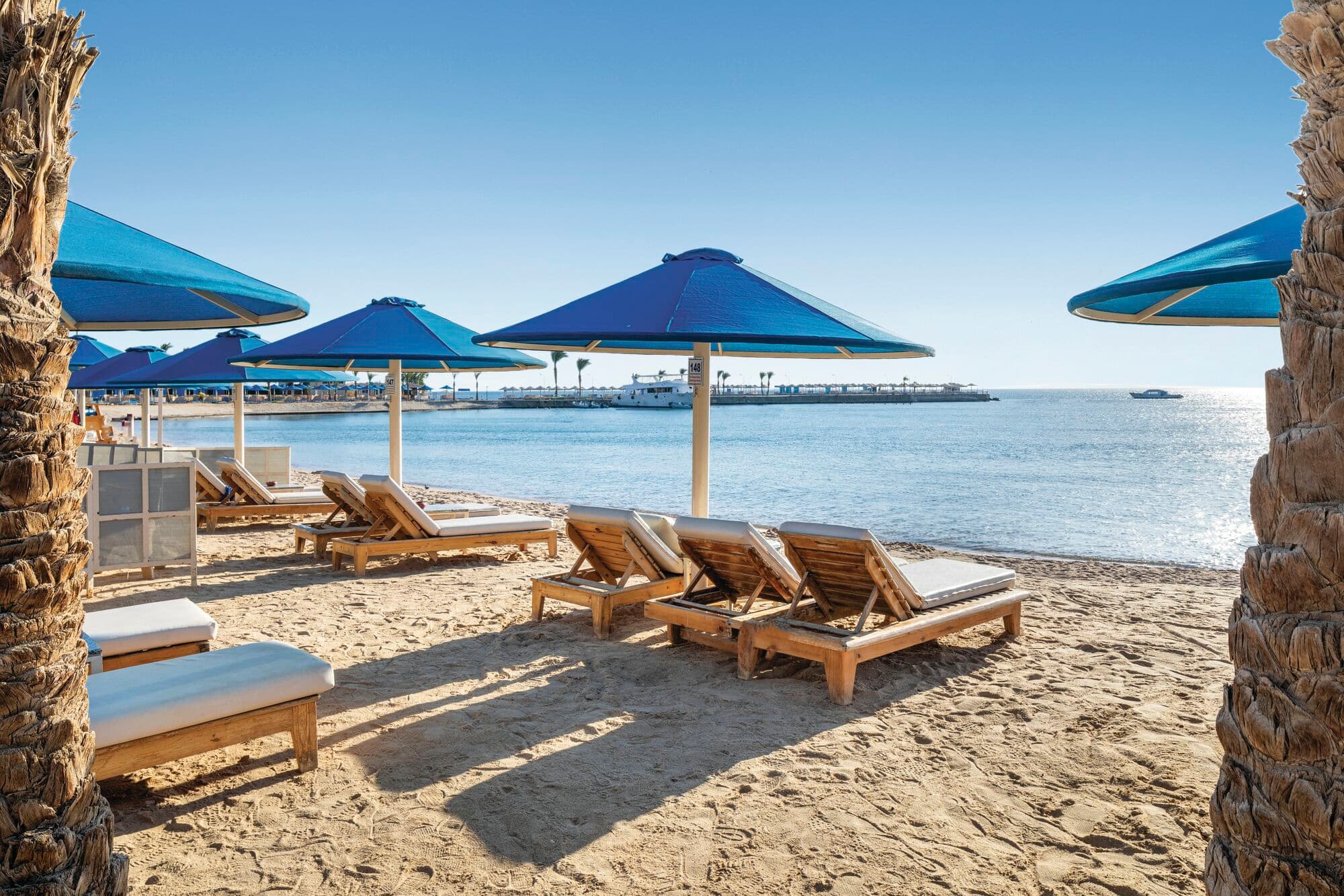 Sunloungers with blue parasols on a sandy beach.