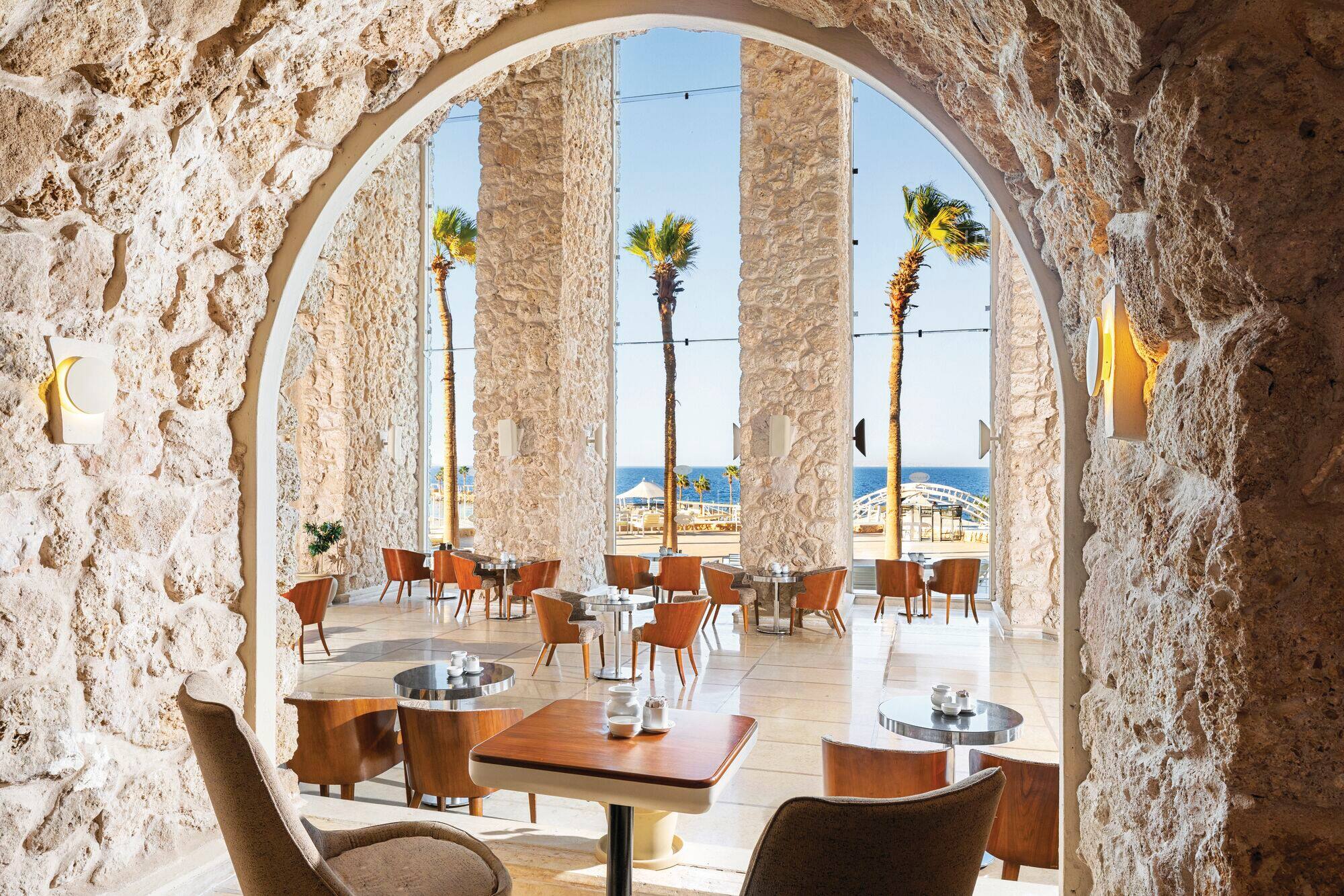 A restaurant seating area with stone arches and a sea view. 