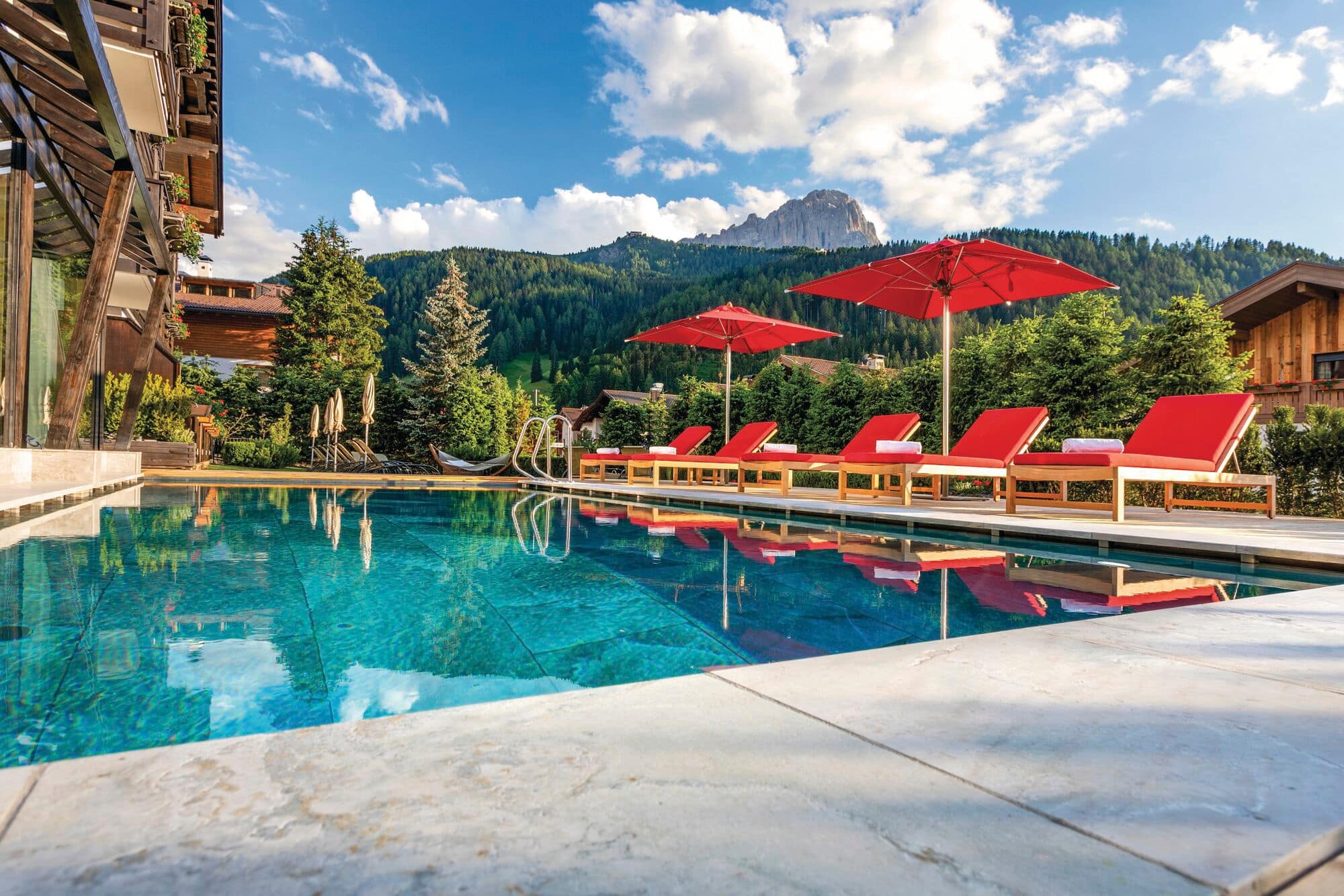 The pool area at Hotel Tyrol in Selva di Val Gardena, with green mountains in the background.