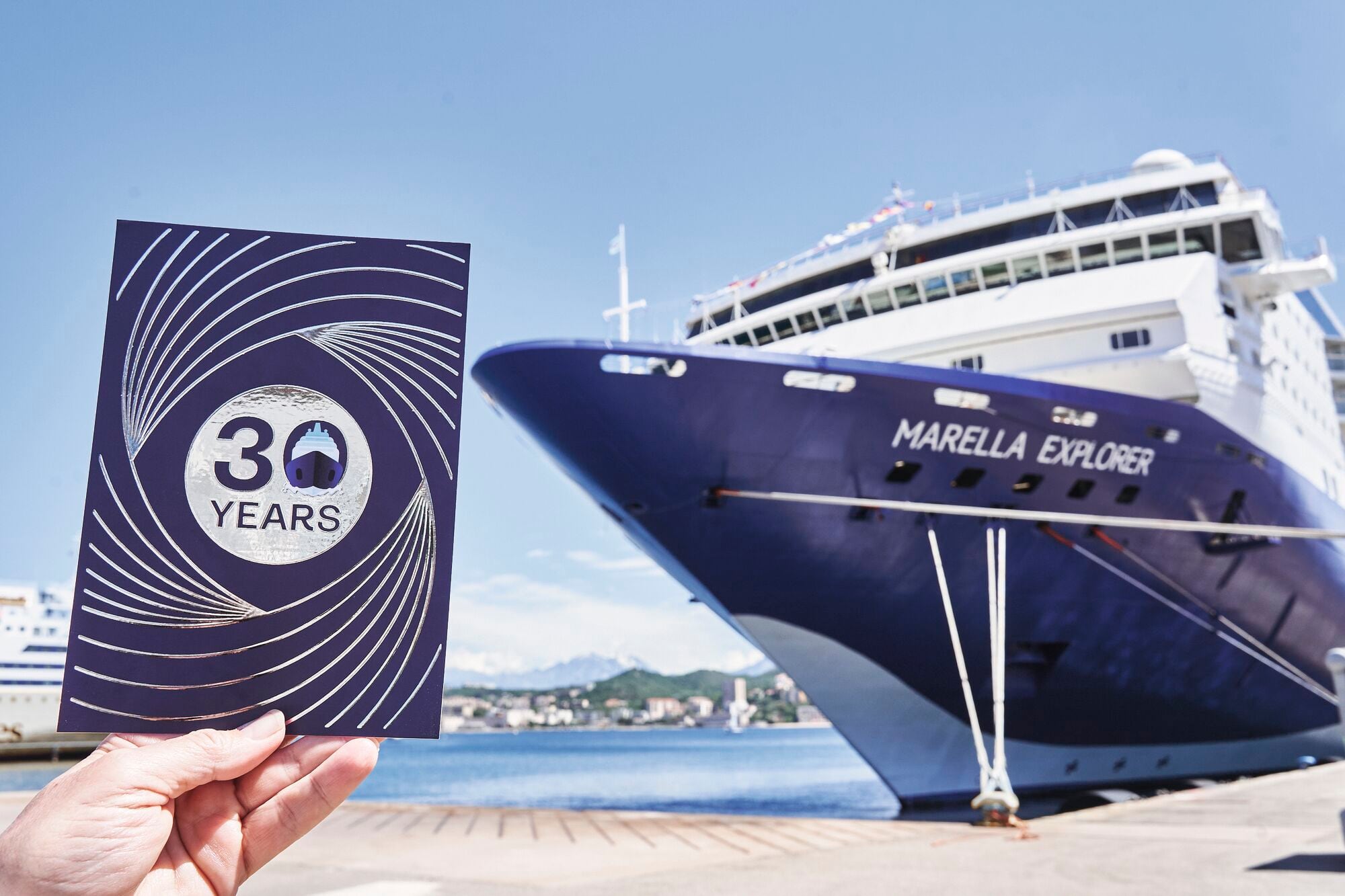 A close-up of a hand holding a 30th birthday card in front of a Marella ship.