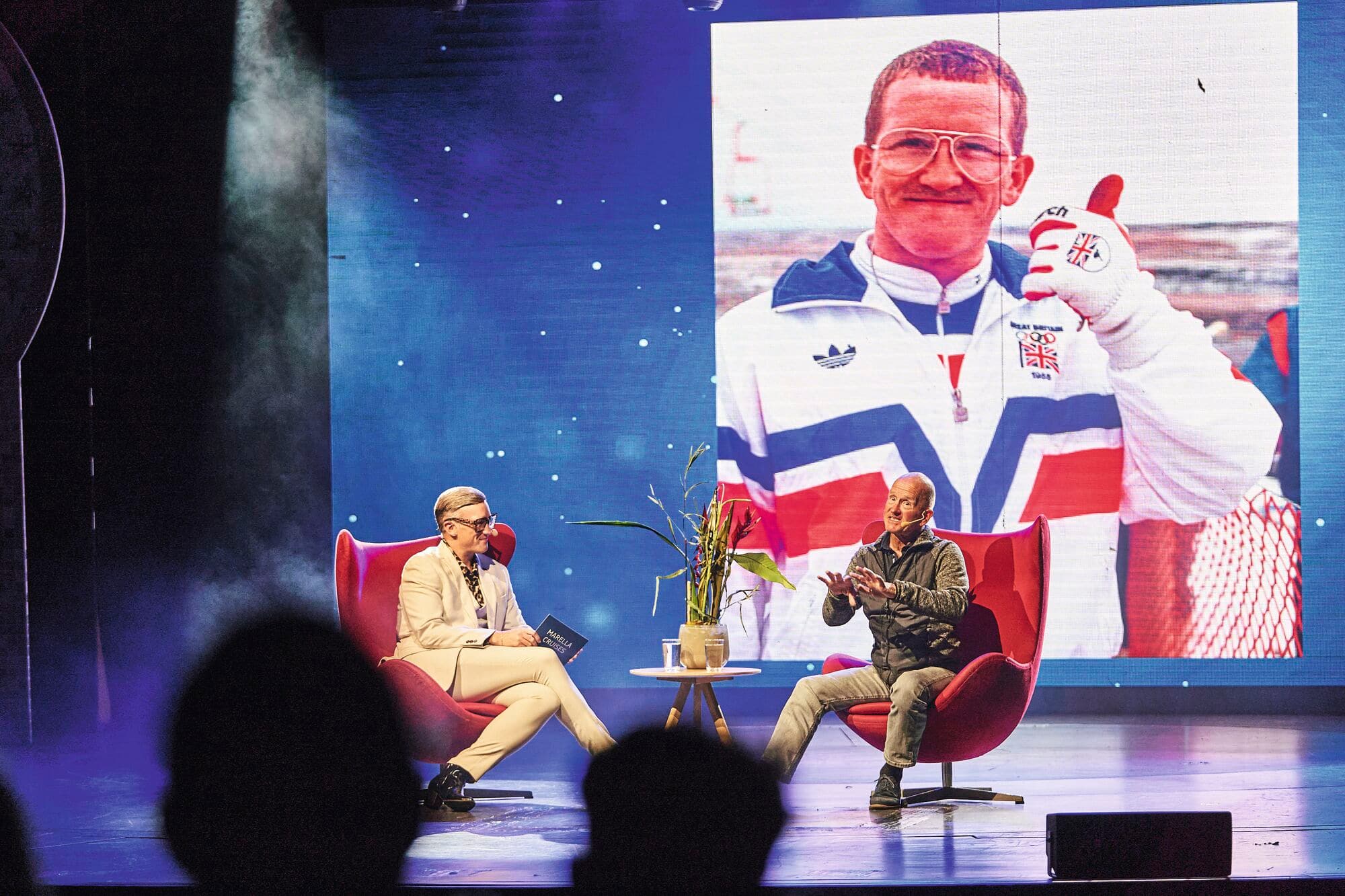 Eddie the Eagle being interviewed on a sofa.