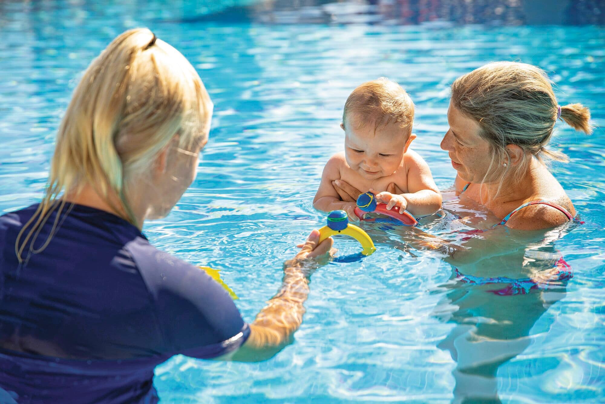 A woman and baby in the water with a swim instructor