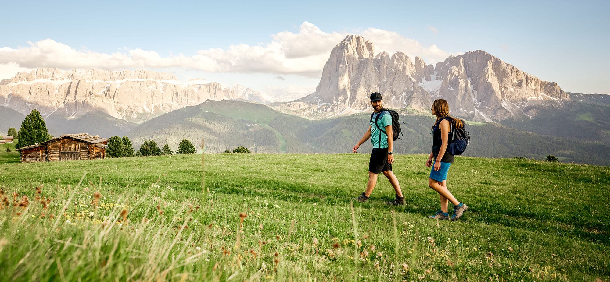 Two people walking across the grassy meadows of Alpe di Suisi in the Dolomites, Italy. 