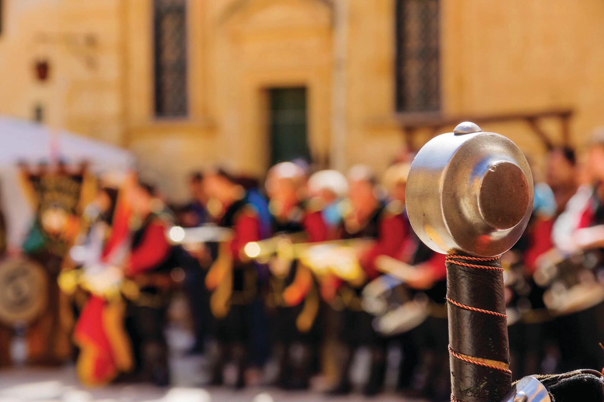 Close-up of a sword hilt with a crowd of medieval reenactors blurred in the background during the Mdina Festival