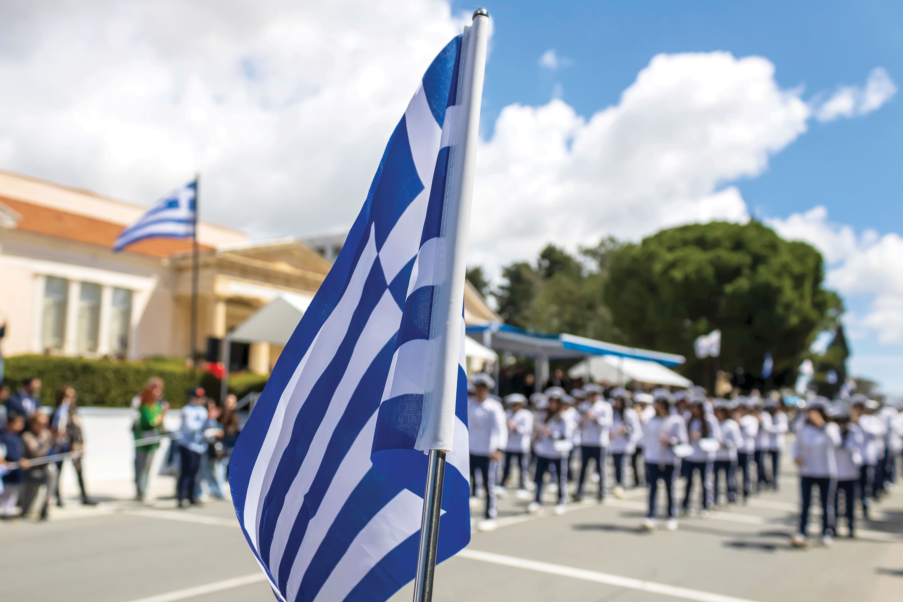 Greek flag in front of brass band marching on Greek Independence Day parade