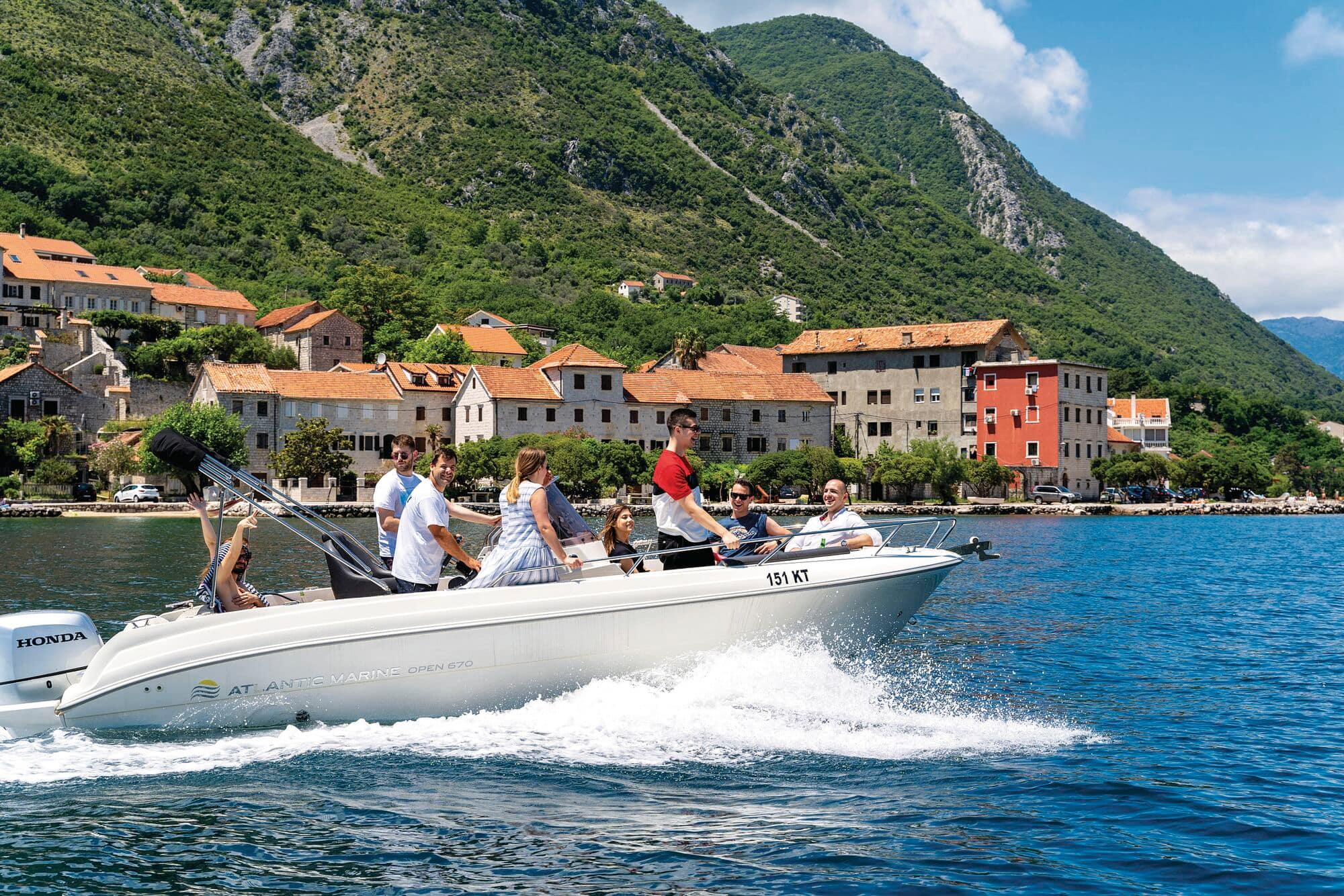 A group of people enjoying a speedboat ride by a hillside town.