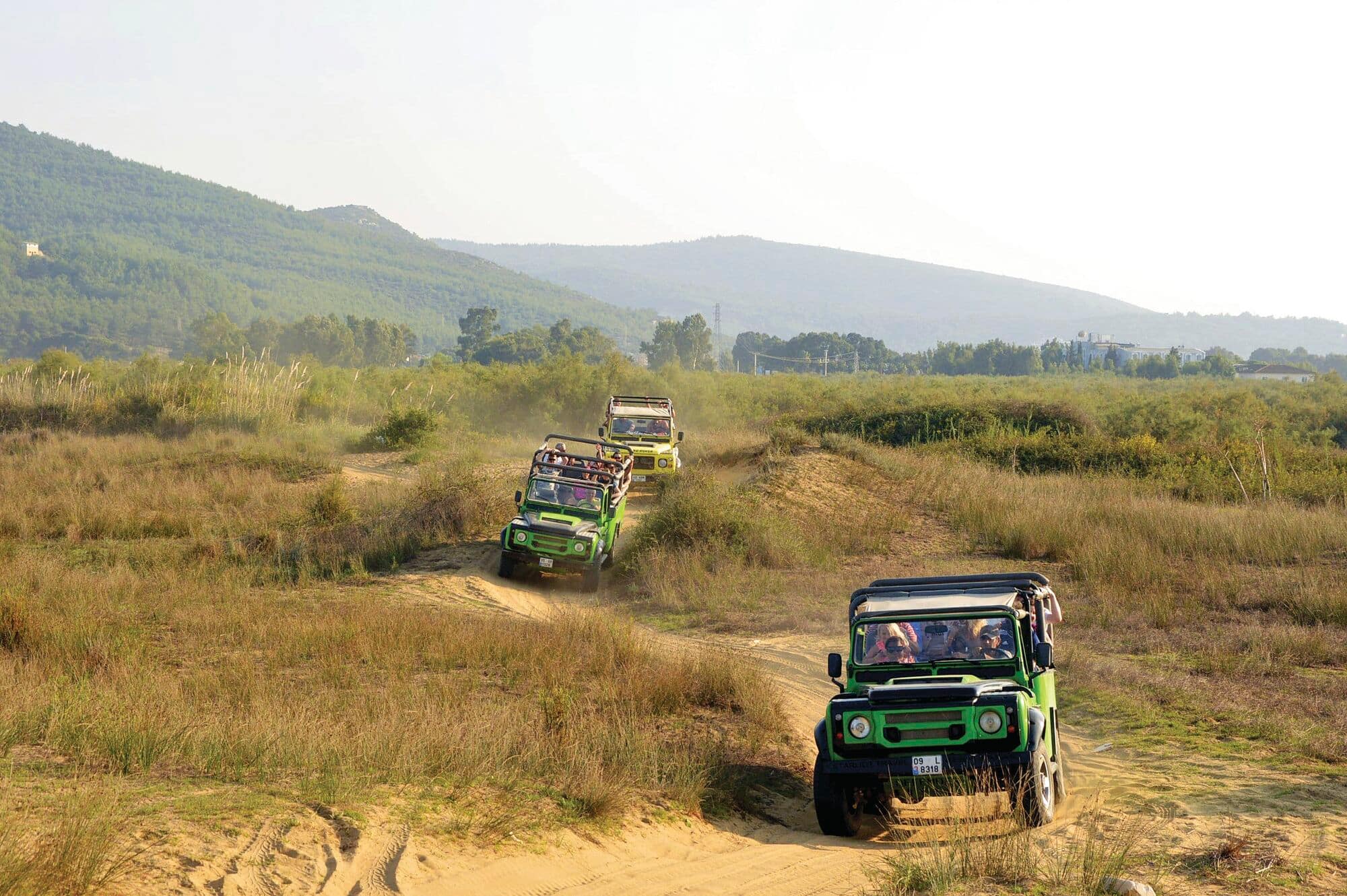 Two bright green off-road vehicles driving on a dirt track through grassland.