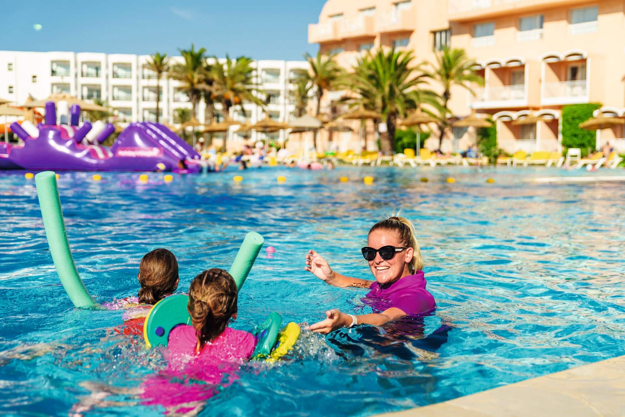 Two children and an instructor taking part in a swim school at a hotel pool.