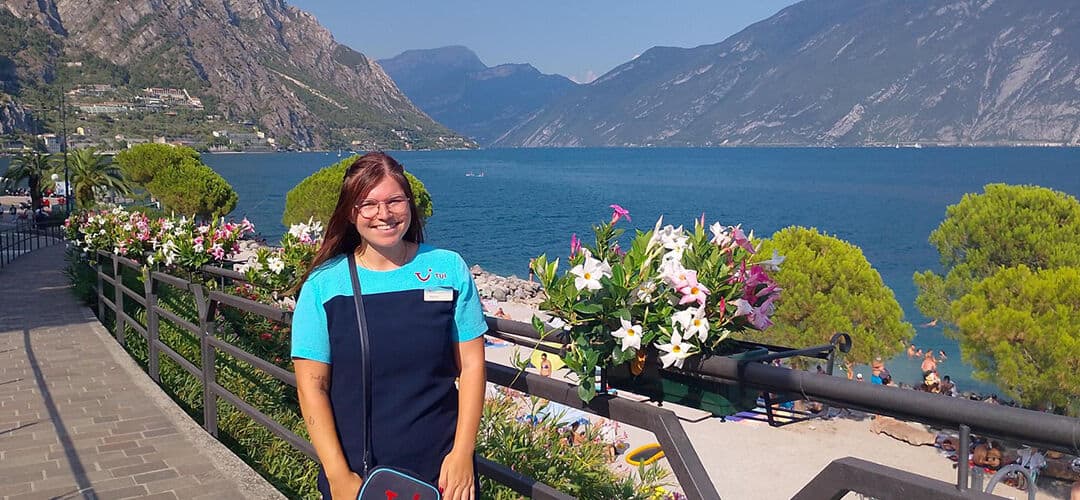 A brown haired woman stands in front of a lake. 