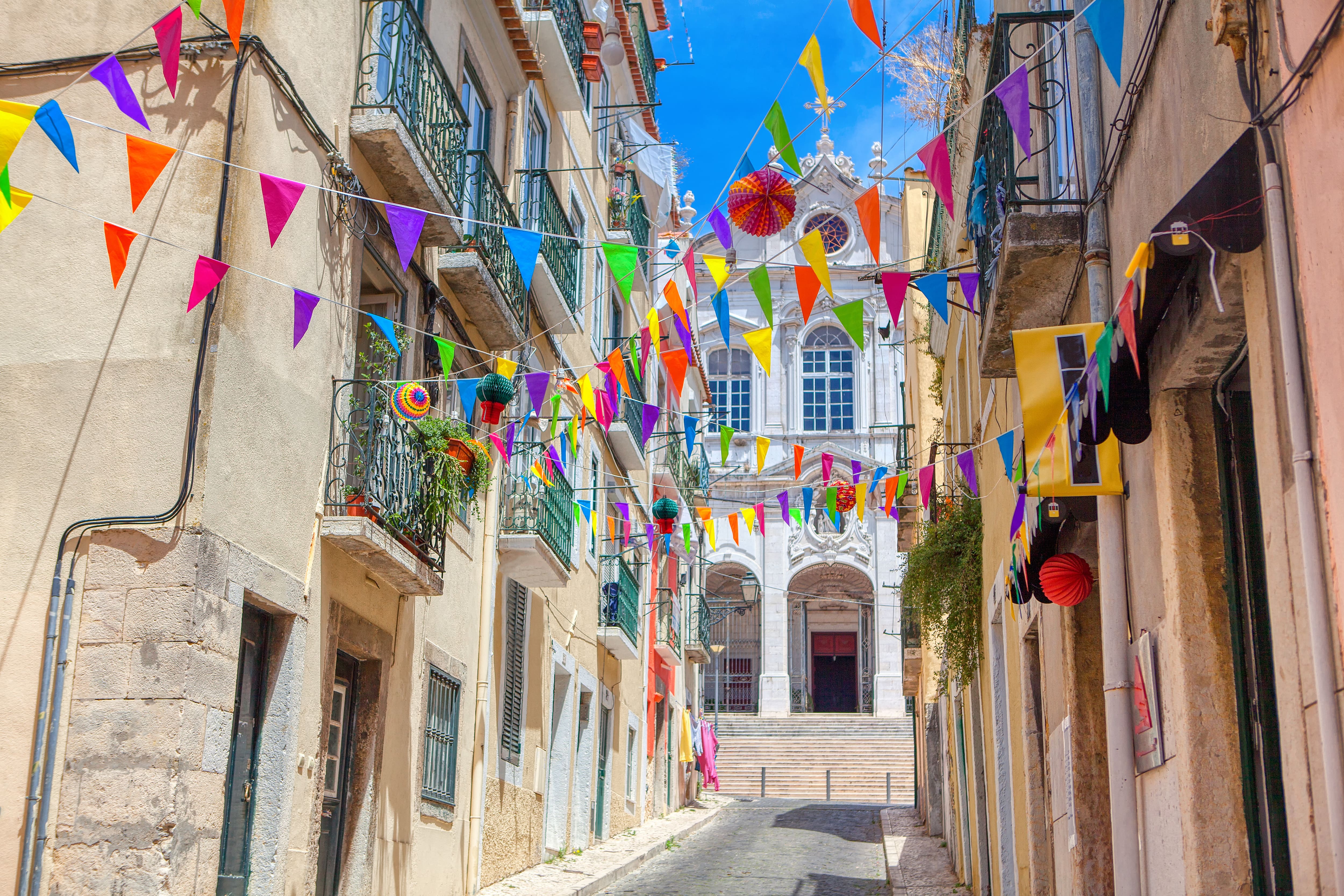 A narrow street lined with buildings and balconies is decorated with colourful bunting.