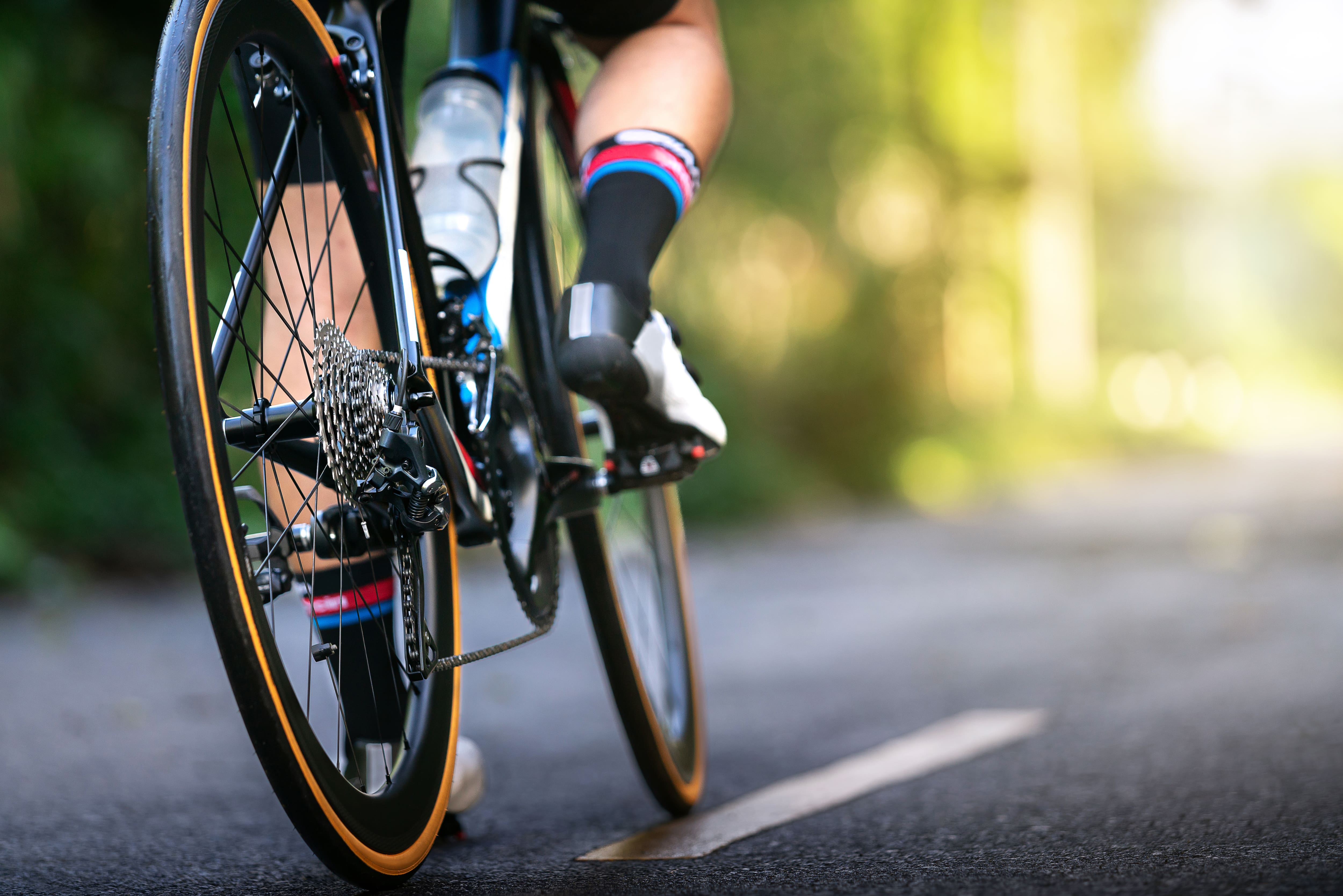 A close-up view of a cyclist riding a road bike on a paved road, with the rear wheel in focus.