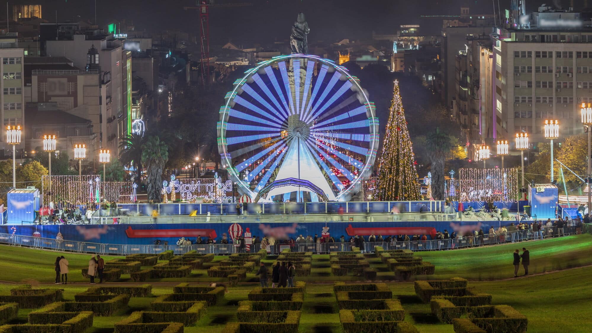 Ferris wheel, Christmas tree and festive lights in a city square at night.
